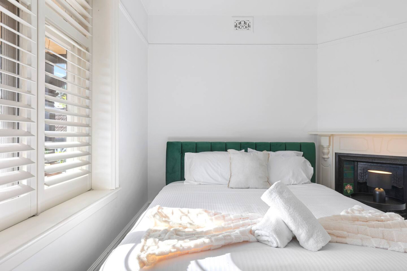 A bright and inviting queen bedroom featuring a luxurious green velvet bed, crisp white linens, and a charming fireplace, creating the perfect blend of comfort and elegance. By Superhostly