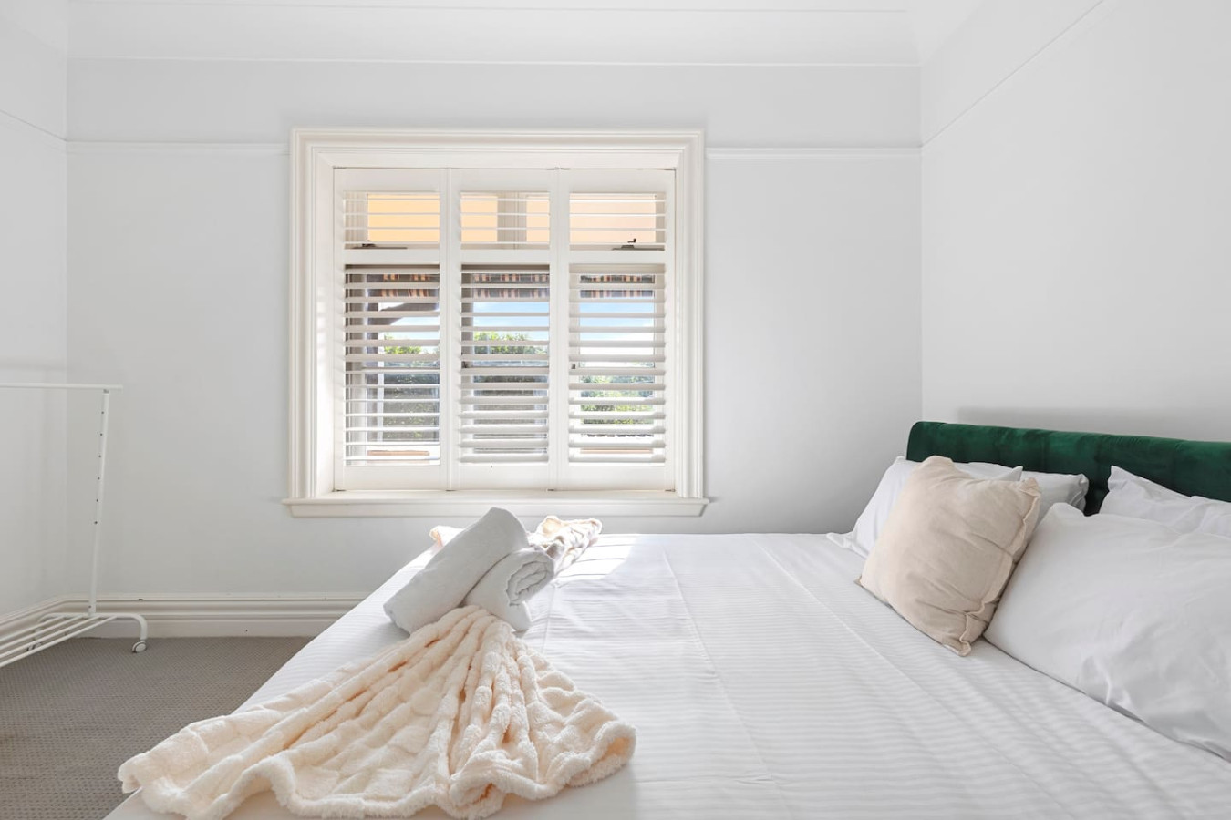 A bright and inviting queen bedroom featuring a luxurious green velvet bed, crisp white linens, and a charming fireplace, creating the perfect blend of comfort and elegance. By Superhostly
