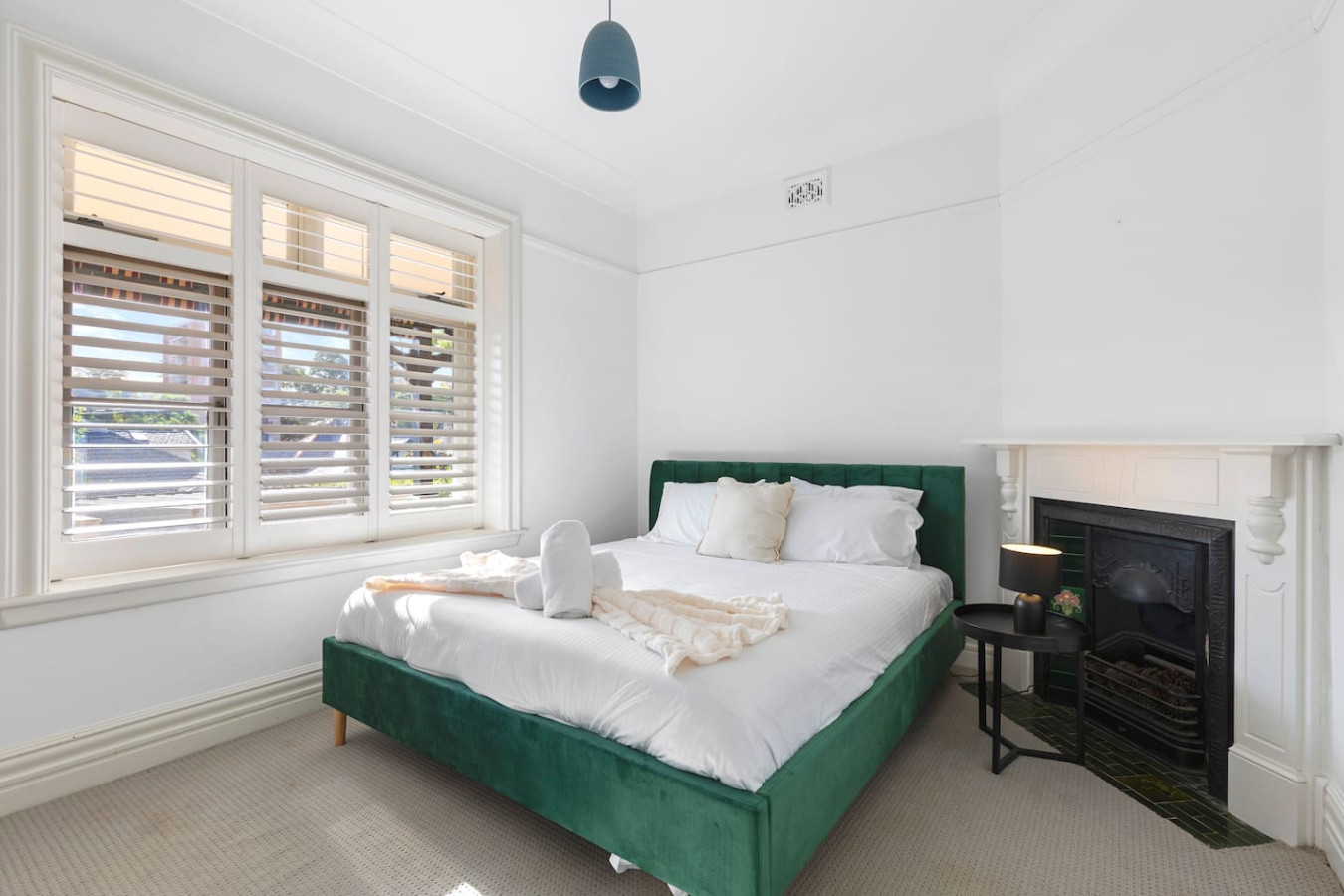 A bright and inviting queen bedroom featuring a luxurious green velvet bed, crisp white linens, and a charming fireplace, creating the perfect blend of comfort and elegance. By Superhostly