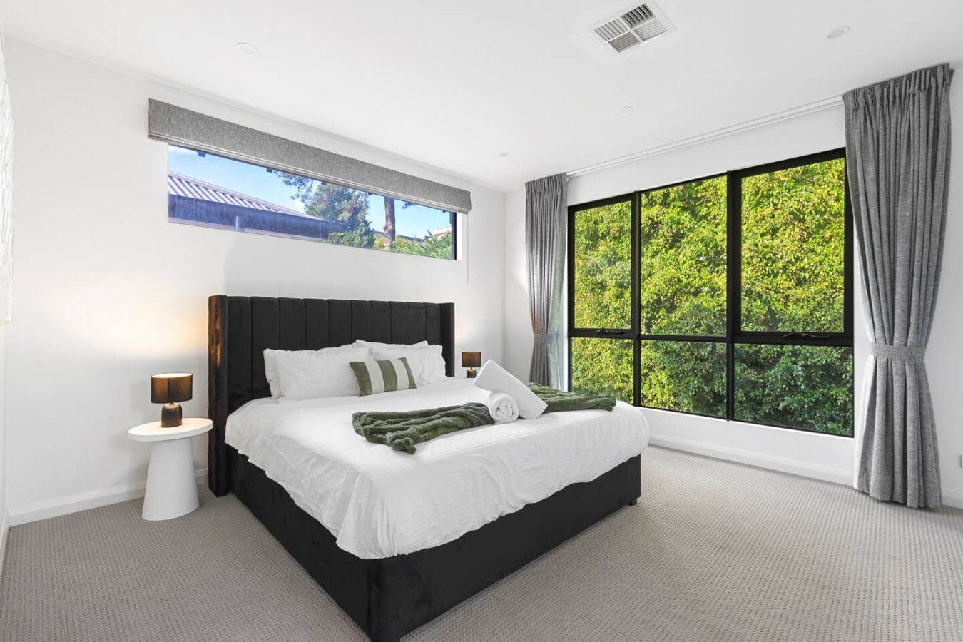 A spacious and modern king bedroom with a luxurious king-size bed, large windows allowing natural light to flow in, and a stunning view of lush greenery. By Superhostly