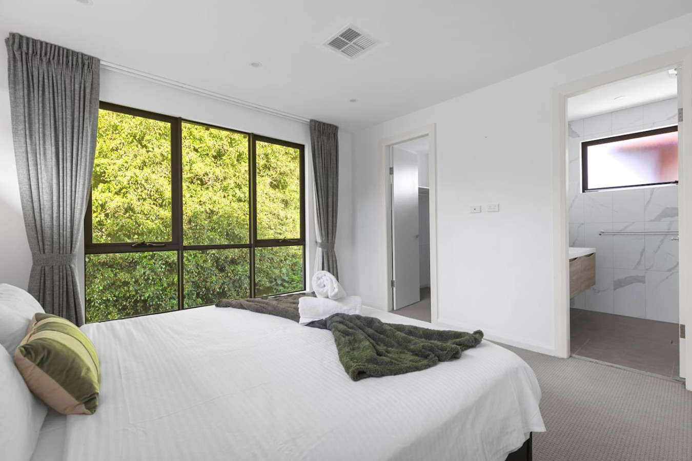 A spacious and modern king bedroom with a luxurious king-size bed, large windows allowing natural light to flow in, and a stunning view of lush greenery. By Superhostly