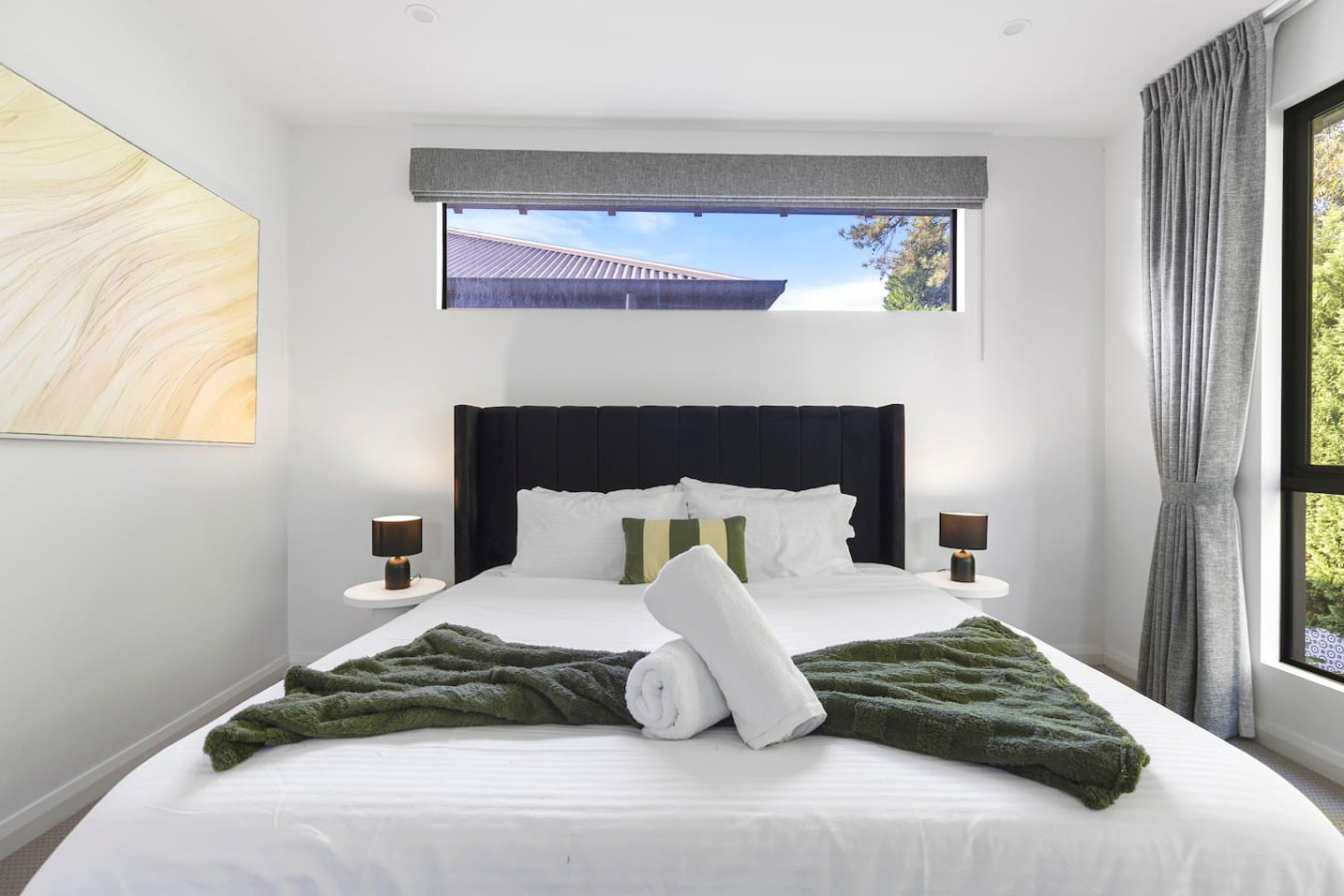 A spacious and modern king bedroom with a luxurious king-size bed, large windows allowing natural light to flow in, and a stunning view of lush greenery. By Superhostly