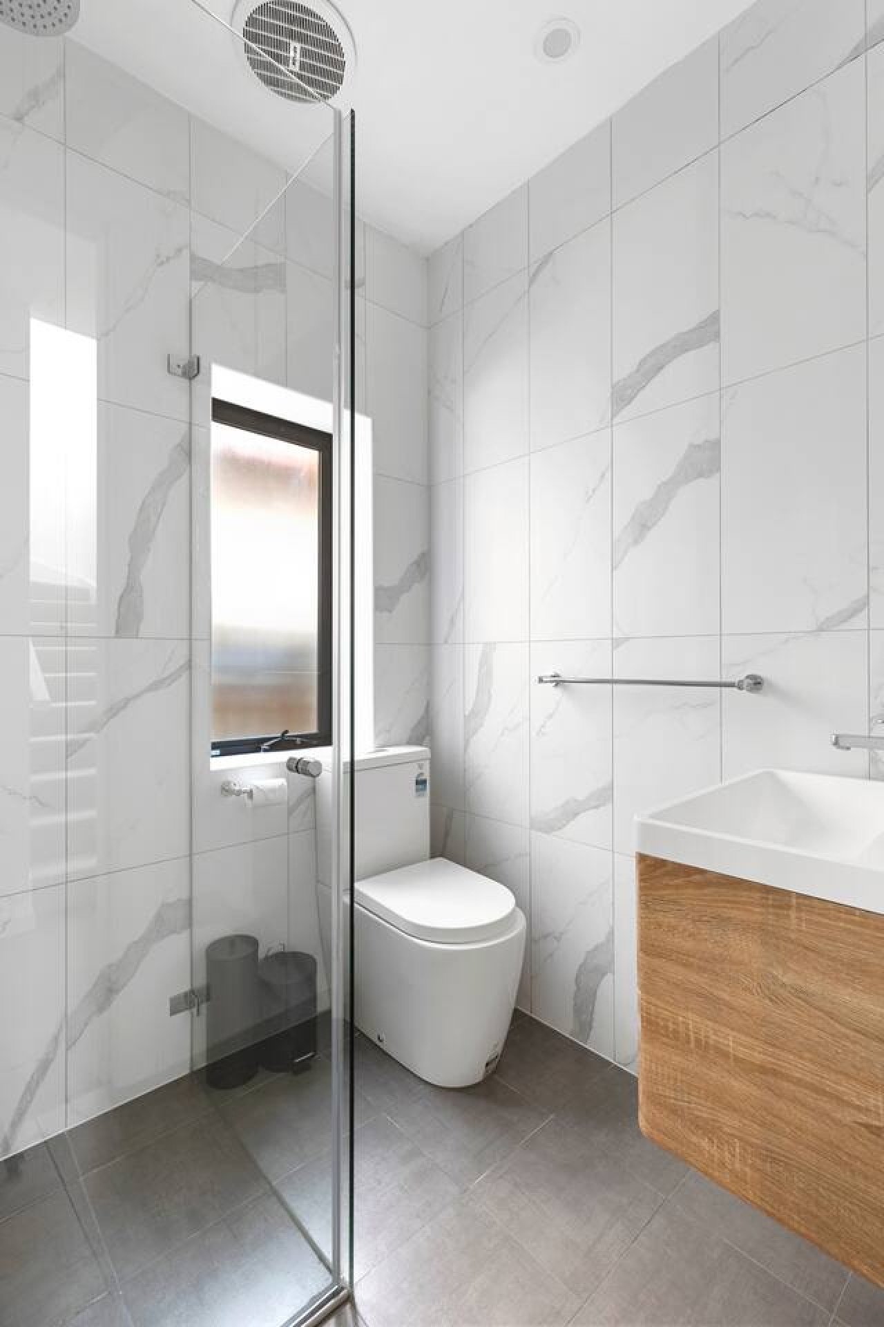 Modern bathroom with sleek marble tiles, a walk-in shower, and stylish wood-accented vanity. By Superhostly