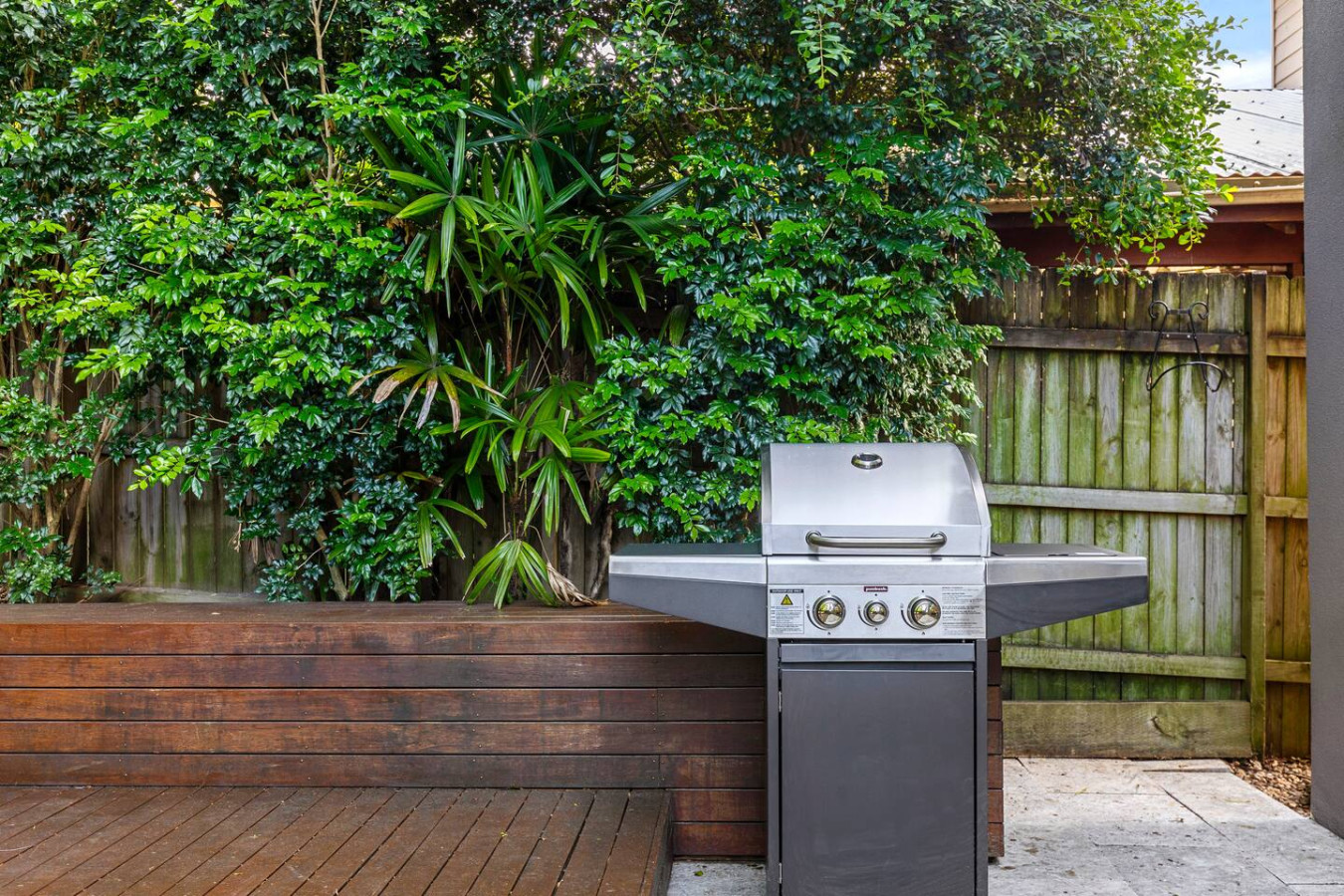 A perfect outdoor setup for summer BBQs, featuring a sleek stainless-steel grill surrounded by lush greenery and a stylish timber deck. By Superhostly