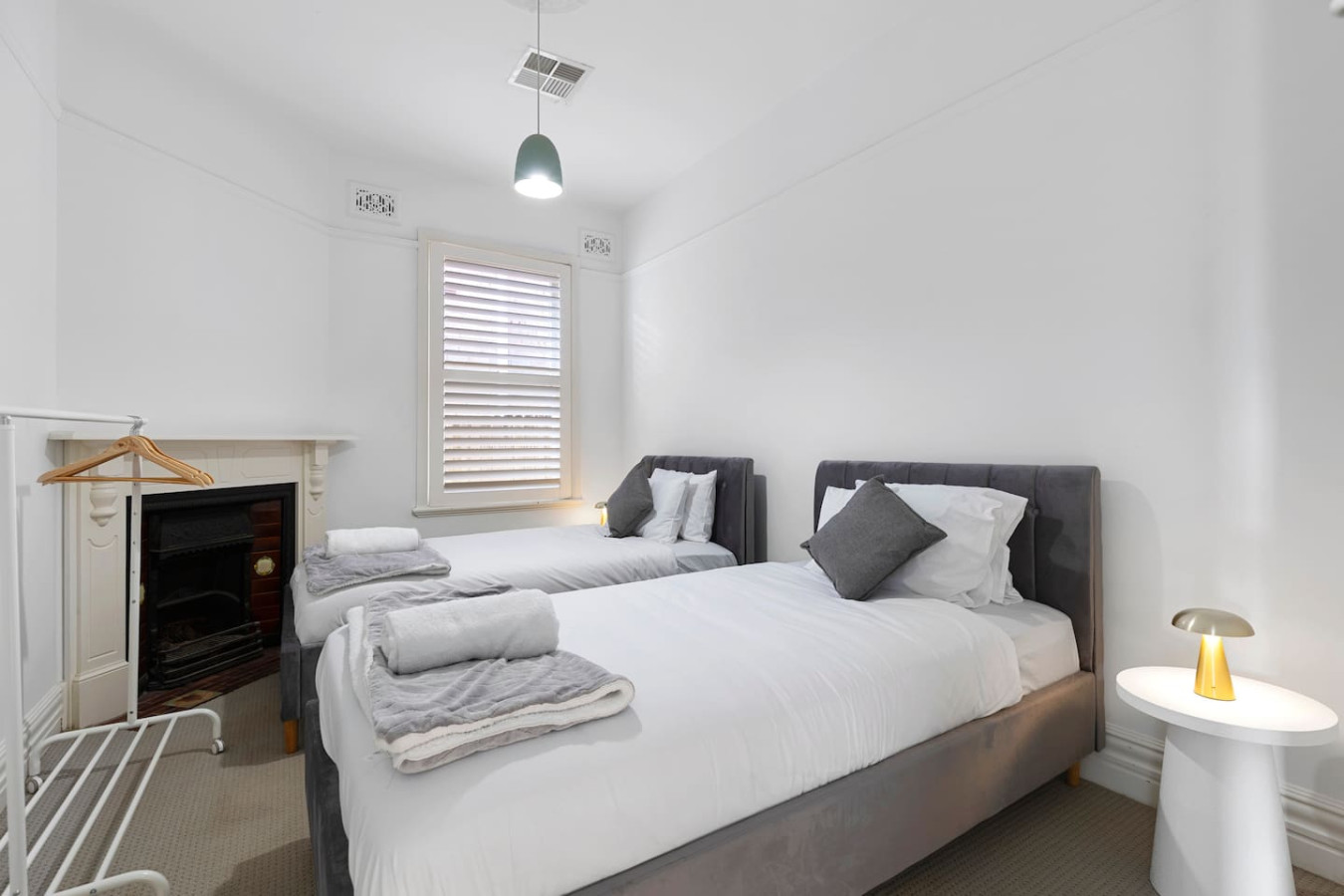 A cozy twin single bedroom featuring two plush single beds with soft gray accents, a charming fireplace, and a warm, inviting atmosphere. By Superhostly
