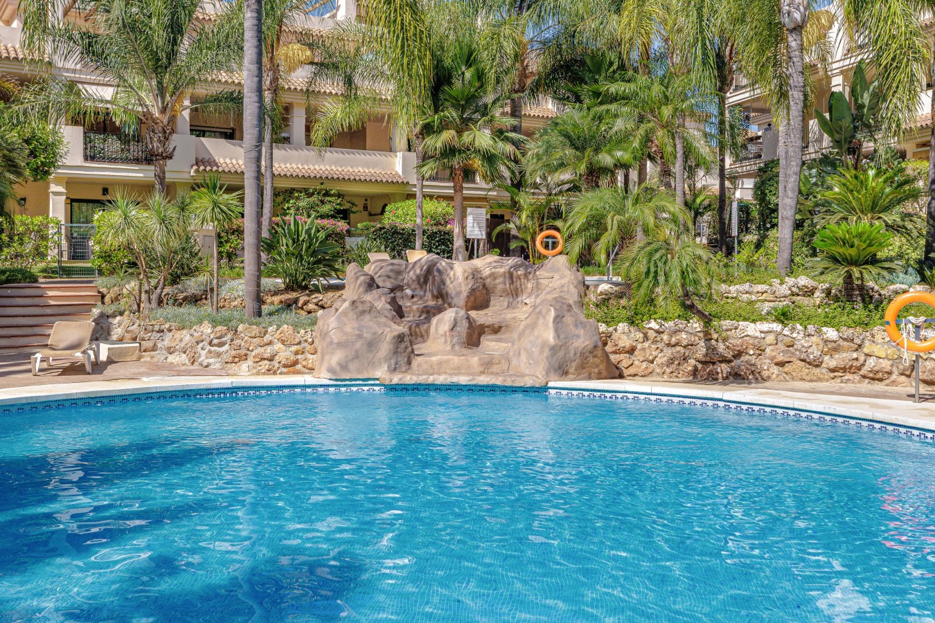 Lagoon style communal pool with rock waterfall, set in tropical gardens