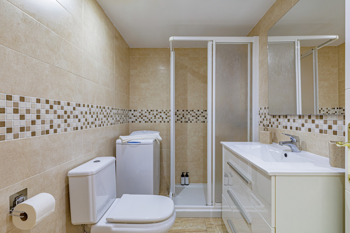 Spotless, modern bathroom featuring a walk-in shower and an in-unit washing machine.