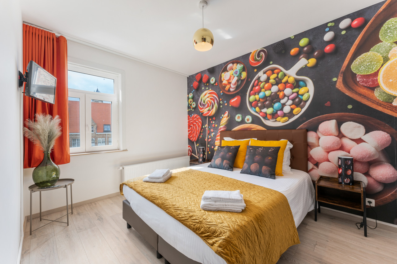 The first bedroom: a wall of sweets behind the double bed, orange curtains, a window and a wall-mounted TV