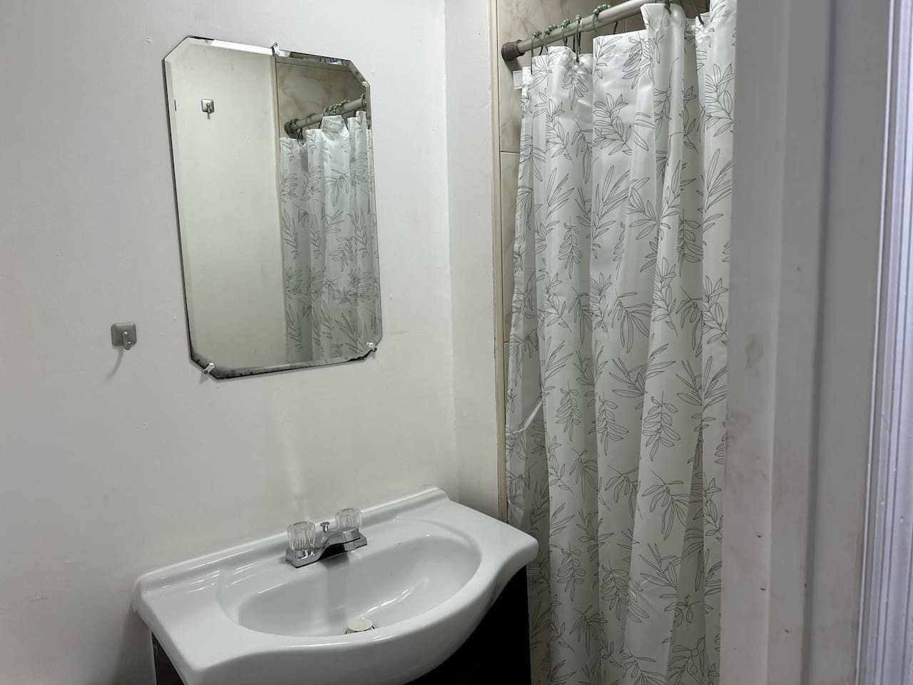Past the shower, a sink and mirror round out this bathroom, with a leaf-print curtain in its own lighter, sketch-style print.