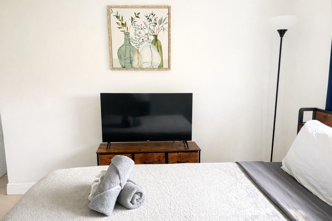 Neutral bedding keeps this room simple, a floor lamp and TV stand rounding out the furniture.