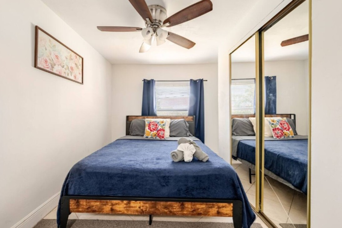Blue bedding and a ceiling fan furnish this bedroom, mirrored closet doors adding storage without eating into the floor space.