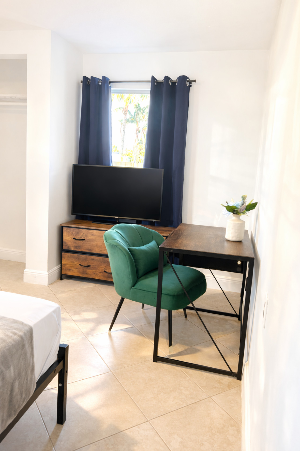 This bedroom corner fits a desk, a TV stand, and another of the same green accent chairs used through the house.