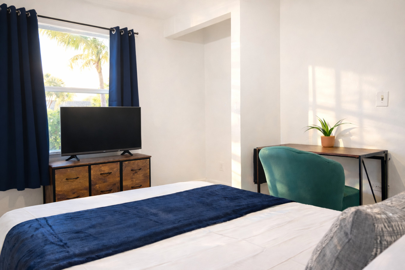 Navy bedding sets this bedroom apart from the others in the house, with a potted plant and TV stand finishing the room.