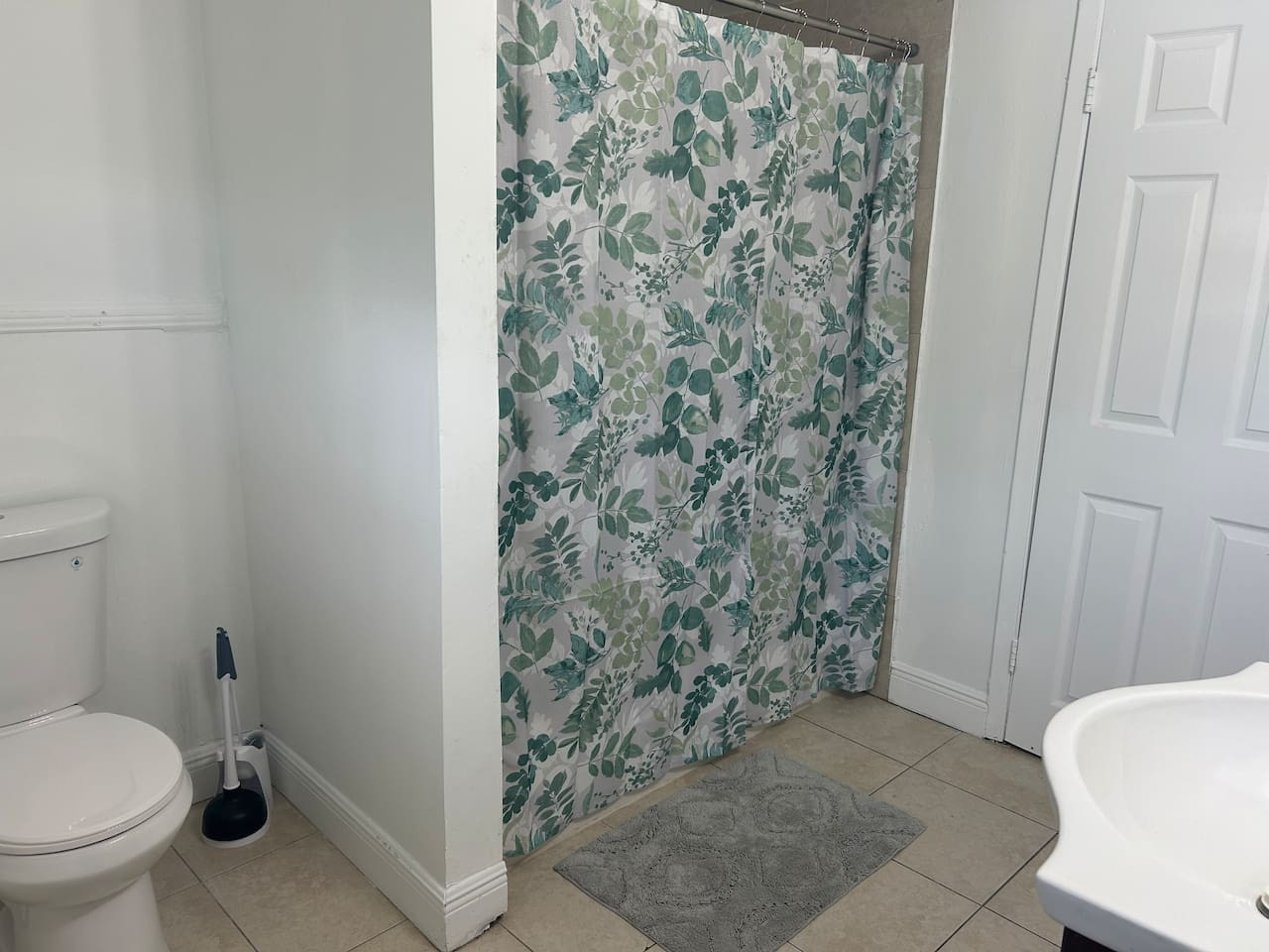 The updated bathroom has a leaf-print shower curtain over a tiled floor.