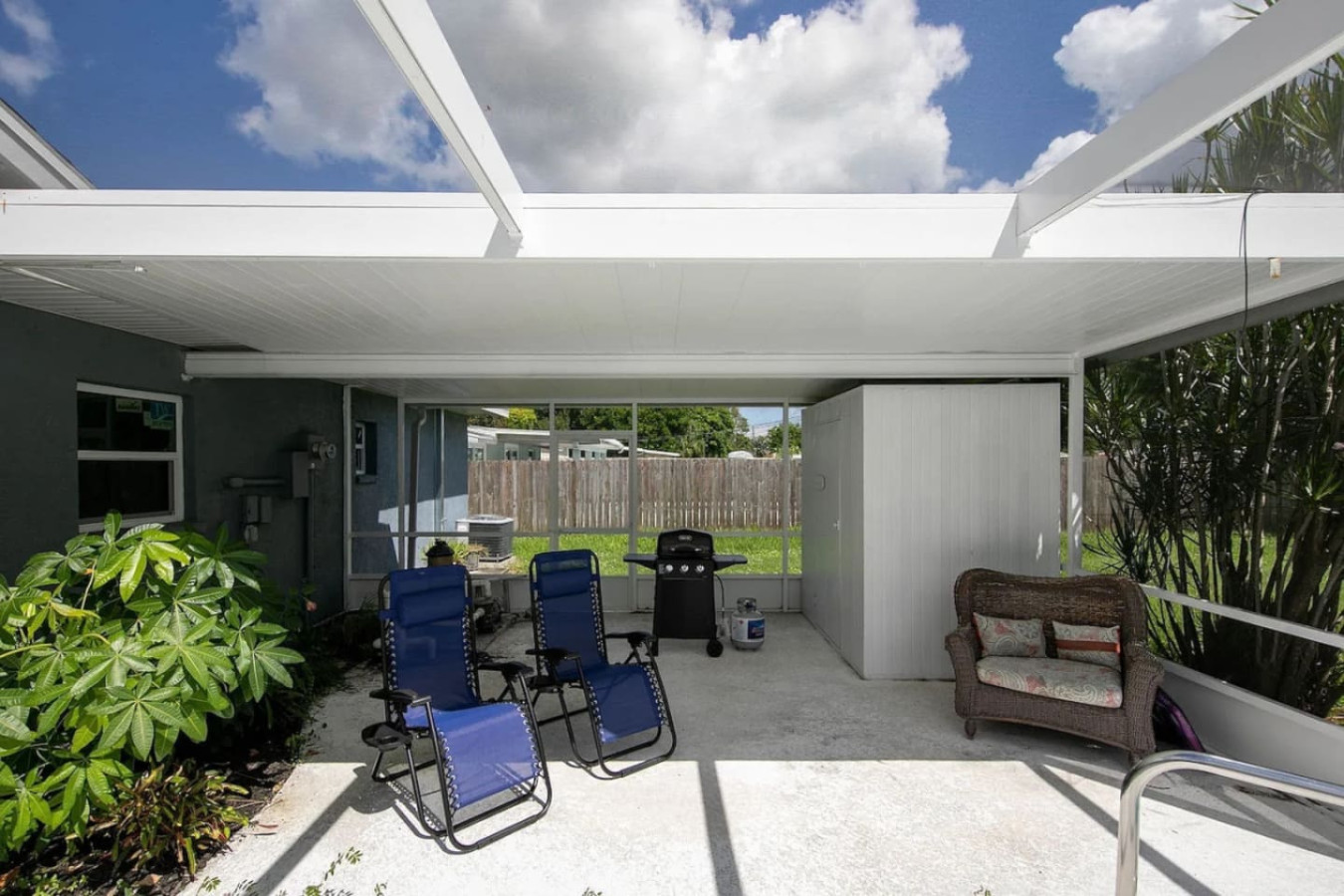 A covered stretch of the patio holds outdoor seating and a grill, shaded for whoever's cooking while everyone else is in the water.