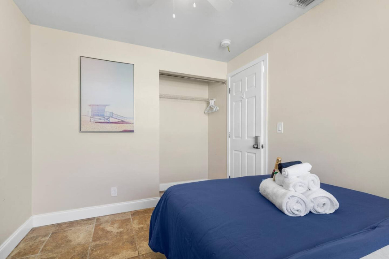 A private bedroom with wall art, a full-size bed, and open closet storage, one of five bedrooms across the house.