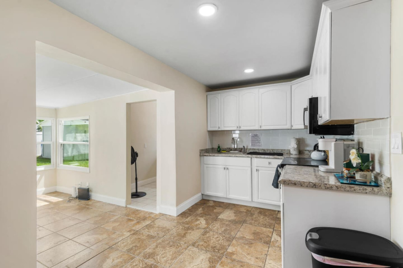 A wider view of the kitchen's white cabinets, opening straight toward the sunroom beyond.