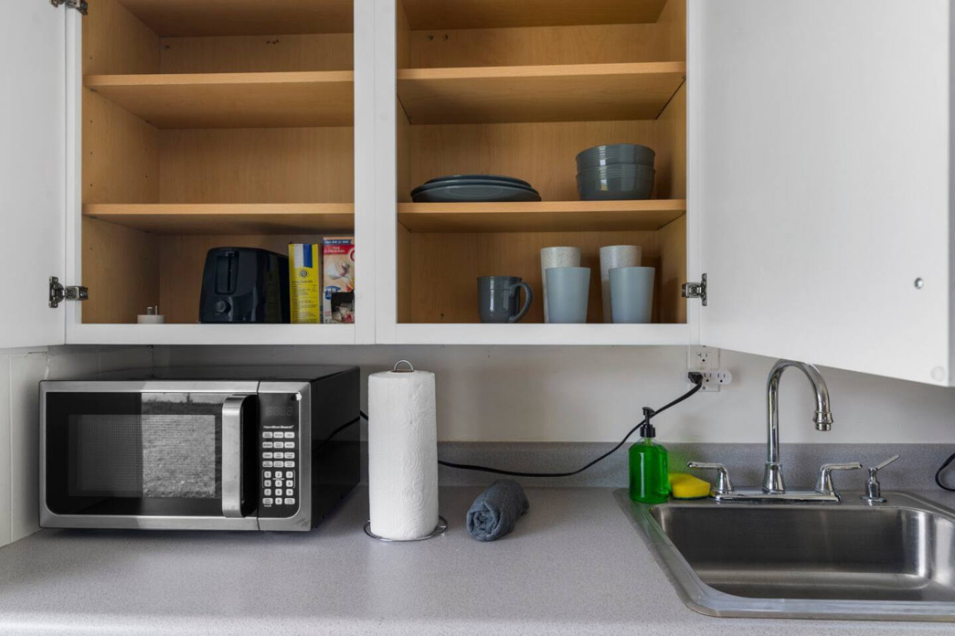A kitchen cabinet stocked with plates, bowls, and mugs, with the microwave tucked underneath.