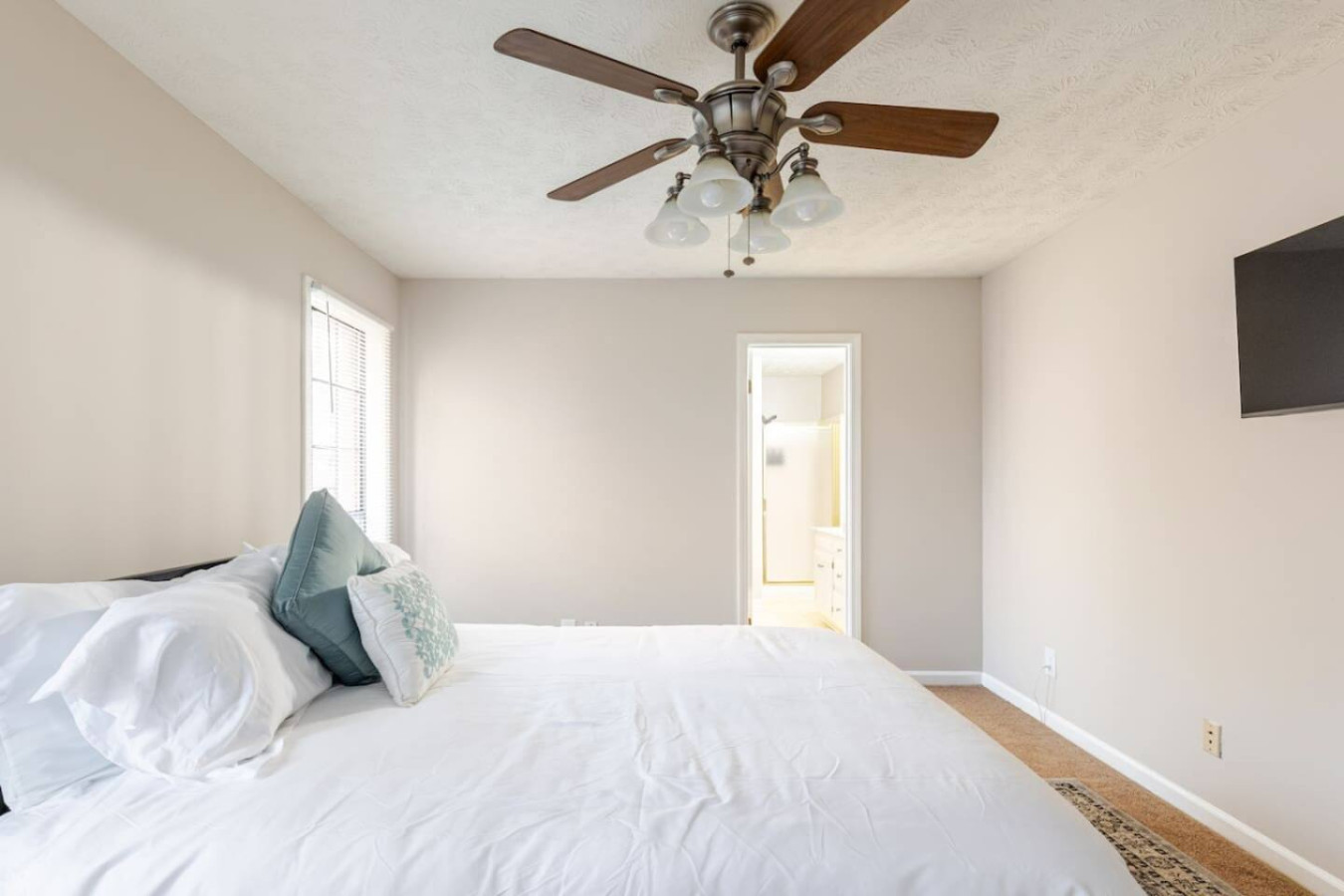 Bedroom 1's queen bed sits under a ceiling fan, with a wall-mounted TV and the private bathroom just through the door.
