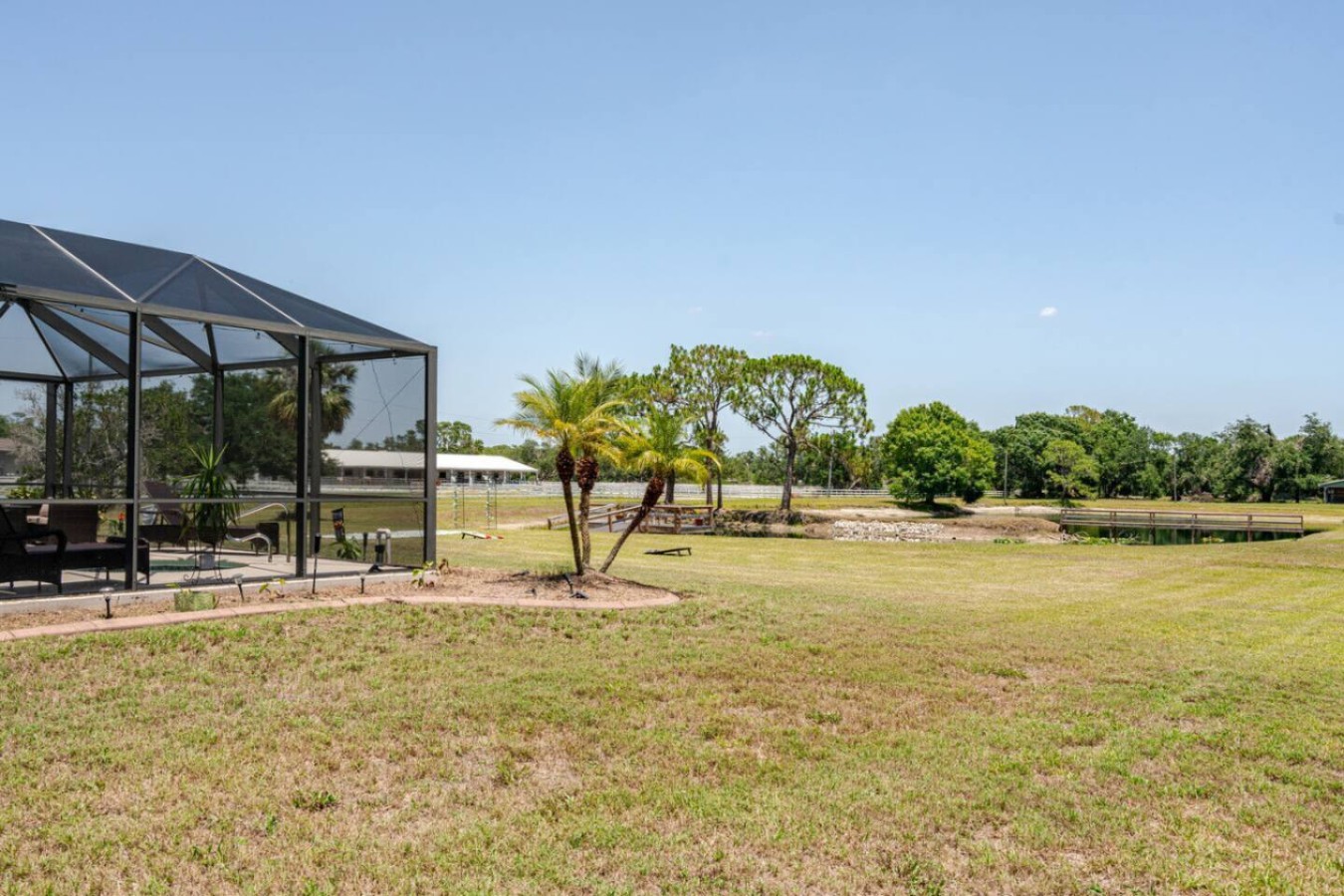 Step off the lanai and the property just keeps going, screened pool in the foreground, the spring-fed pond and a stand of oaks past the treeline.