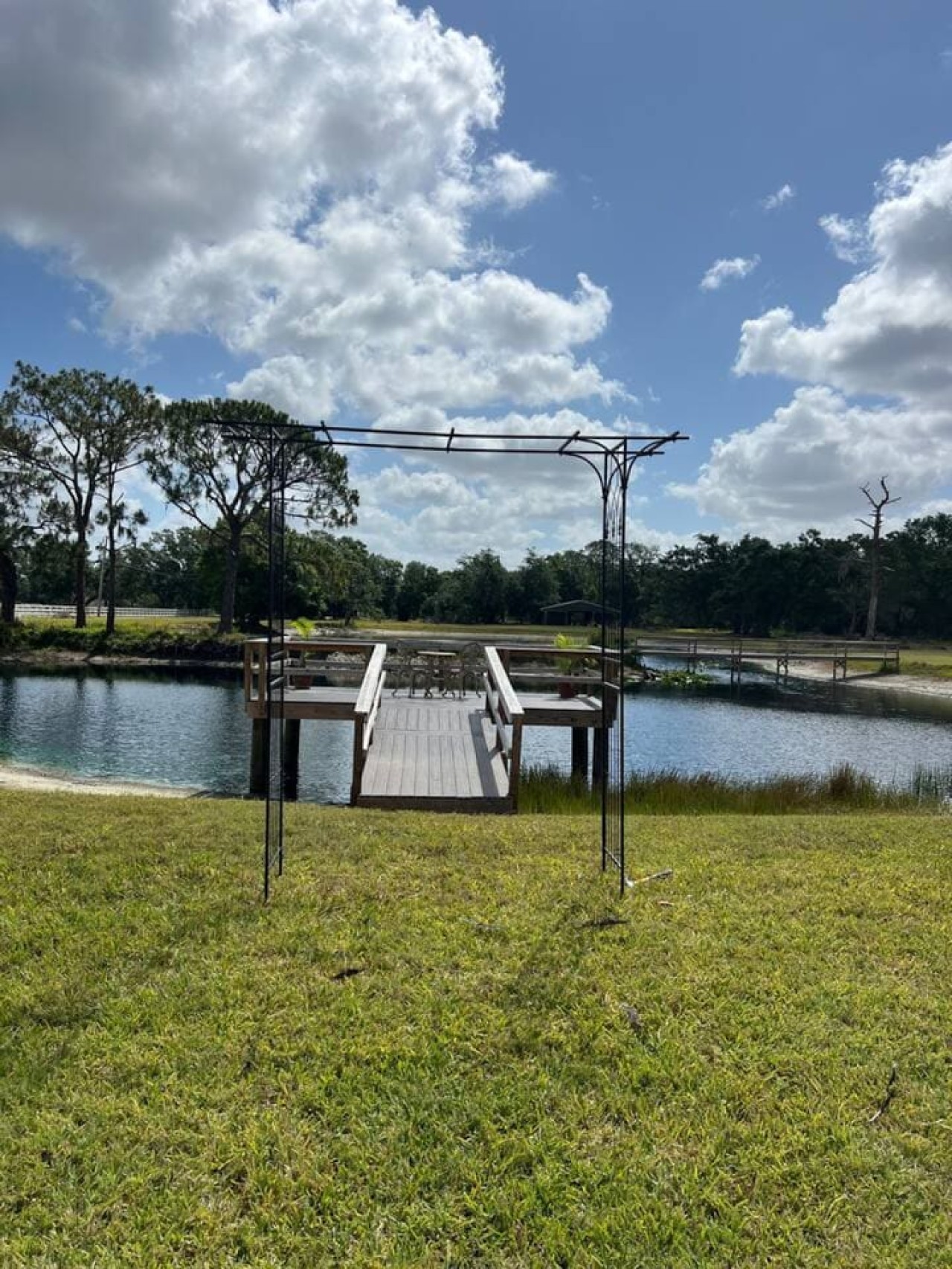 The dock and arbor again, empty, framed by the pond and the tree line behind it.