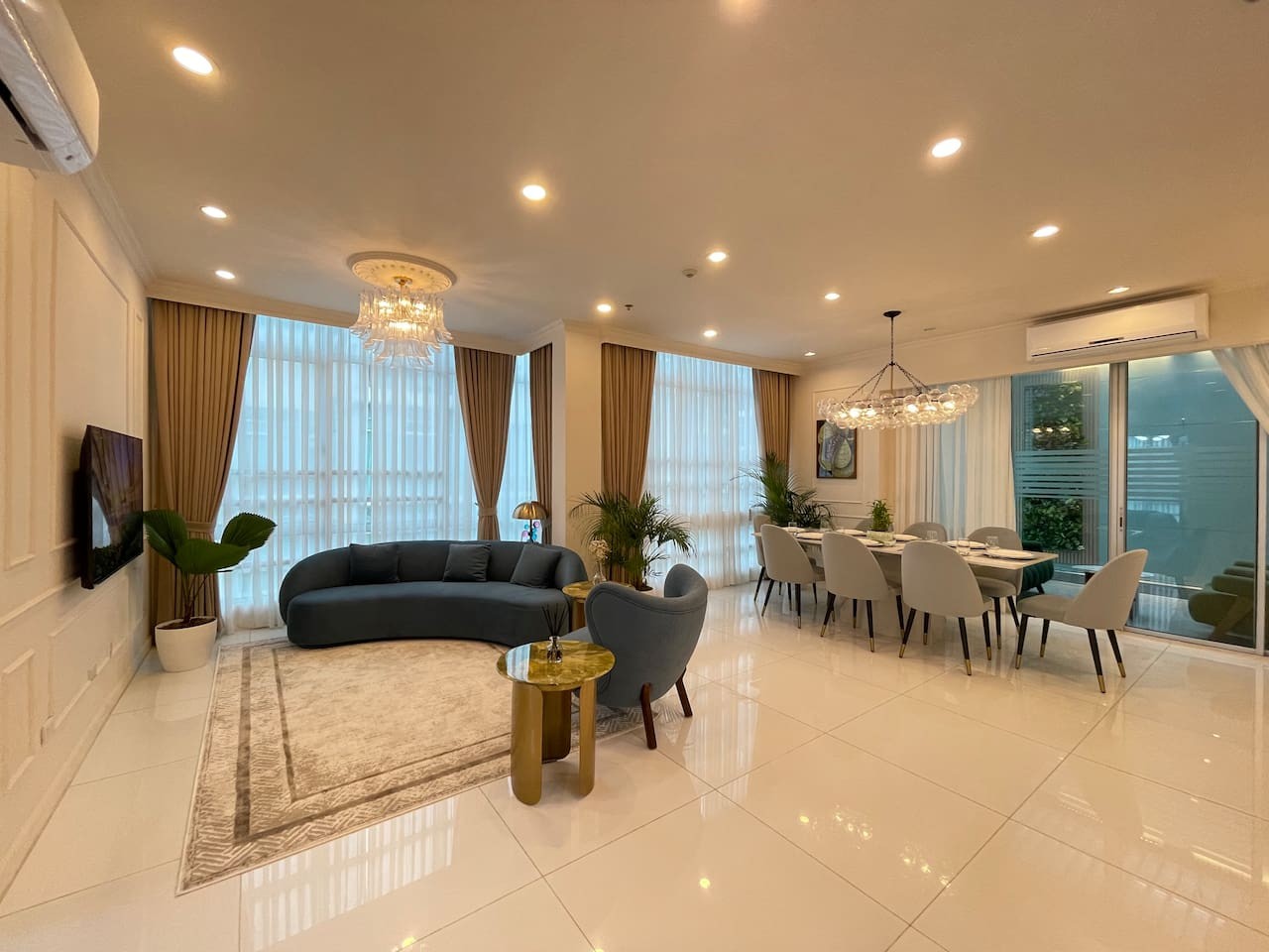 The living area has a sofa and a boucle chair, ideal for relaxation and socializing. It includes a dining table with chairs, and when you add the study table chairs from bedrooms 1 and 2, the space can comfortably accommodate up to 10 guests.