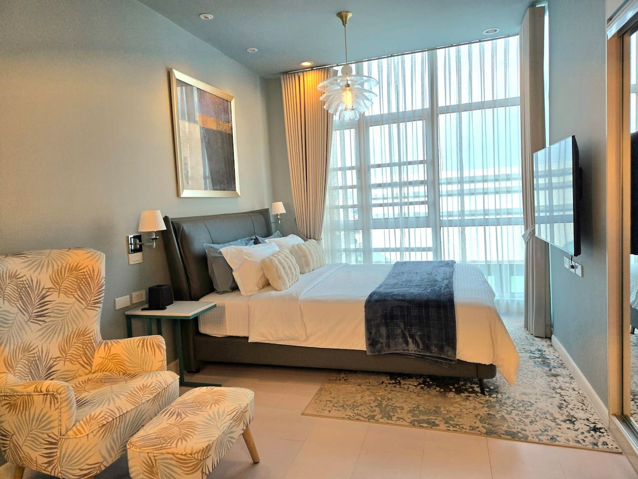 The main bedroom is spacious and relaxing, featuring a cozy queen bed, plush linens, a comfy ottoman chair, and a 55-inch smart TV for your comfort.