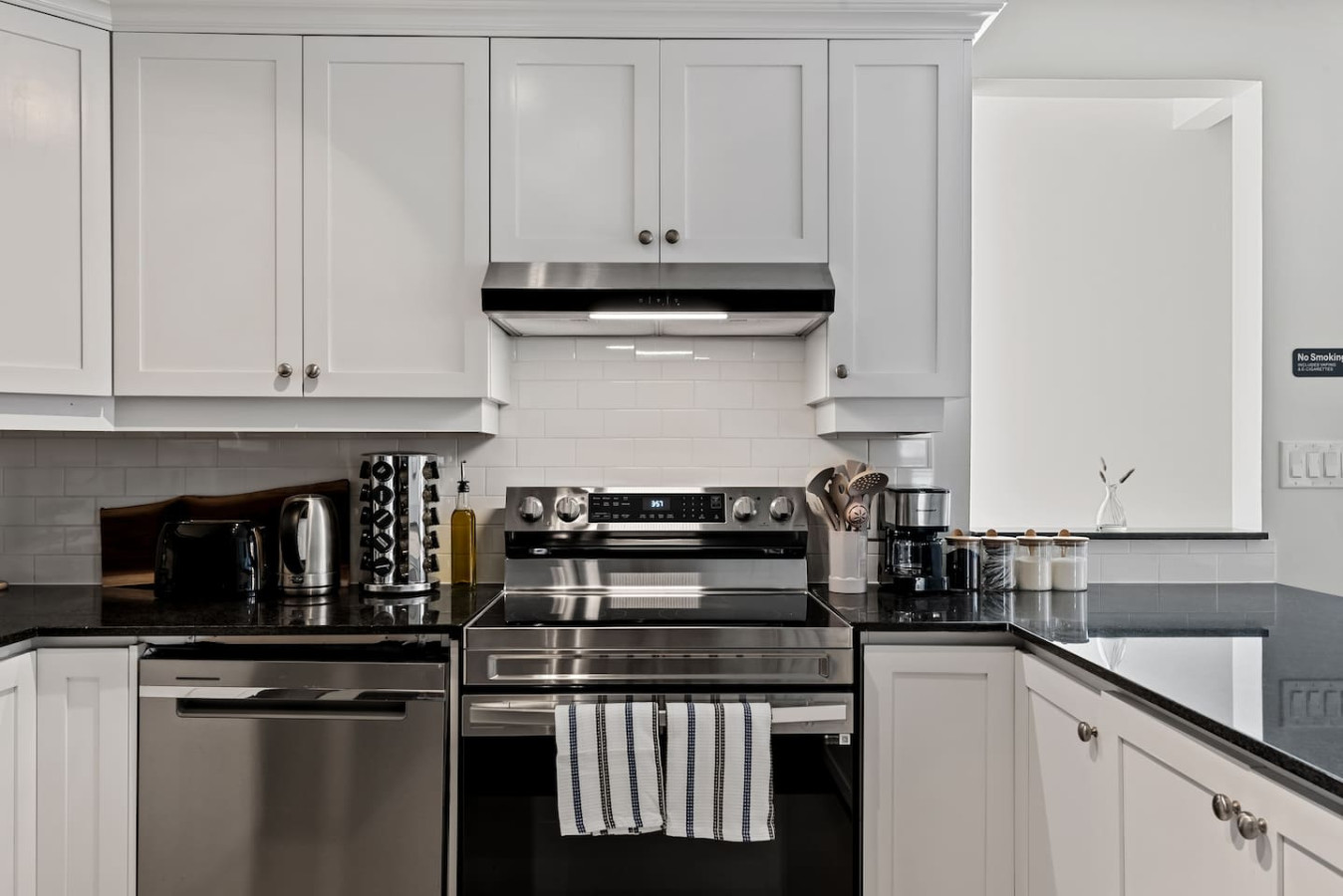 This modern kitchen features a spacious island with cabinetry, sleek white countertops, stainless steel appliances, open shelving, and stylish lighting.