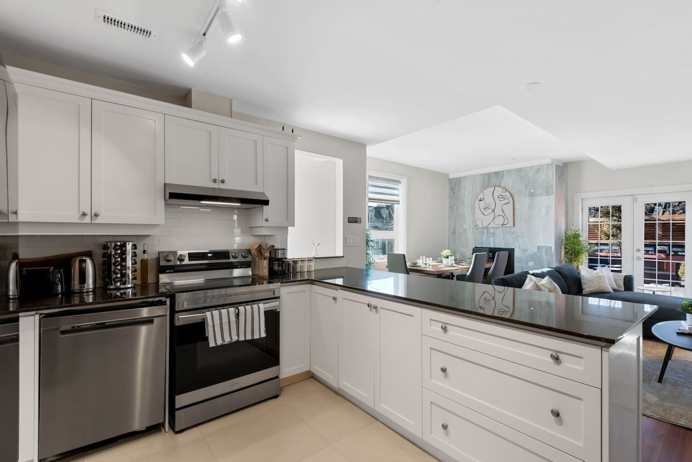This modern kitchen features a spacious island with cabinetry, sleek white countertops, stainless steel appliances, open shelving, and stylish lighting.