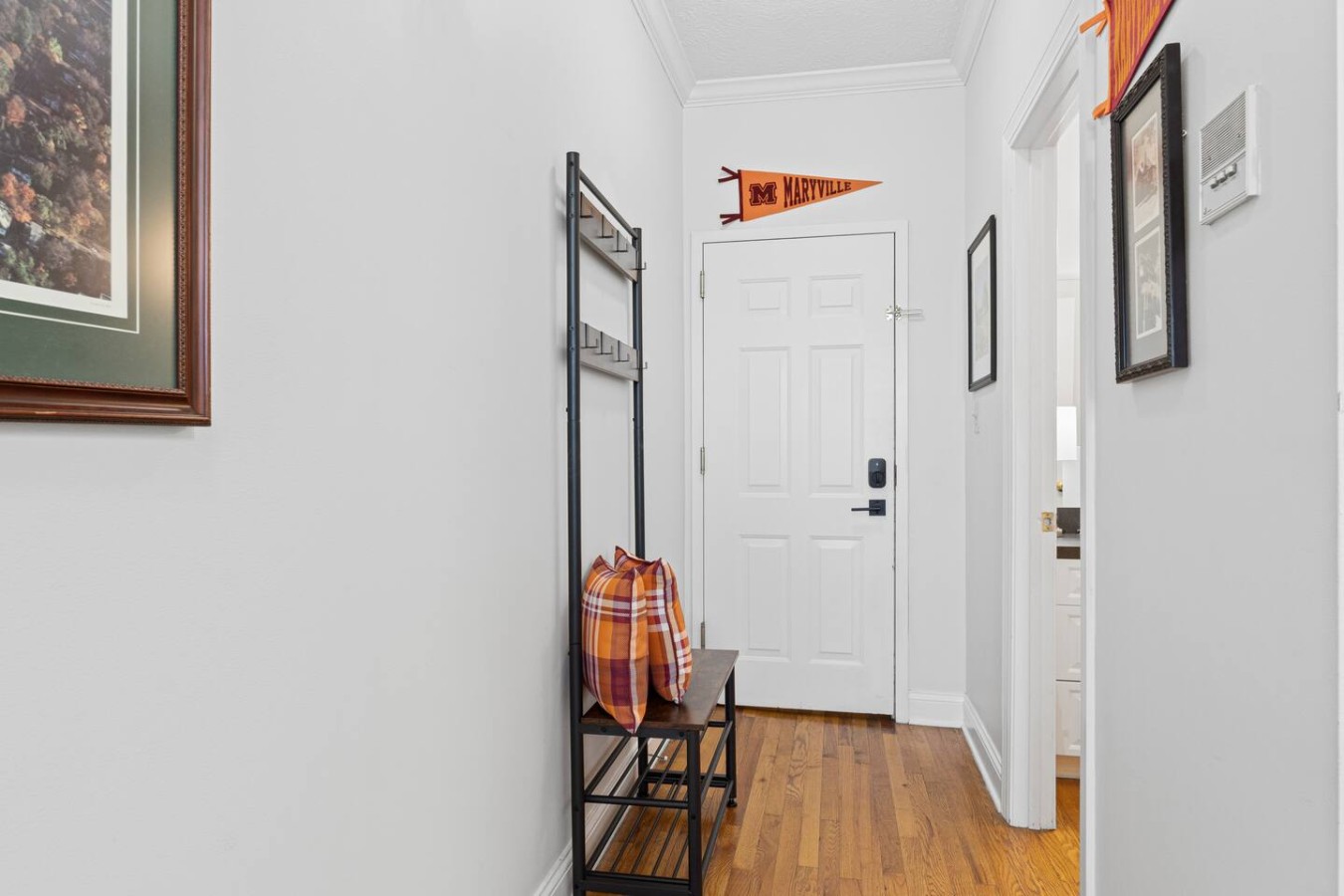 Step into Scots Suite through this welcoming entryway, where you'll find a cozy seating nook with vibrant pillows and handy hooks for your belongings. The suite is full of charming details, including nods to Maryville College, creating a warm and inv