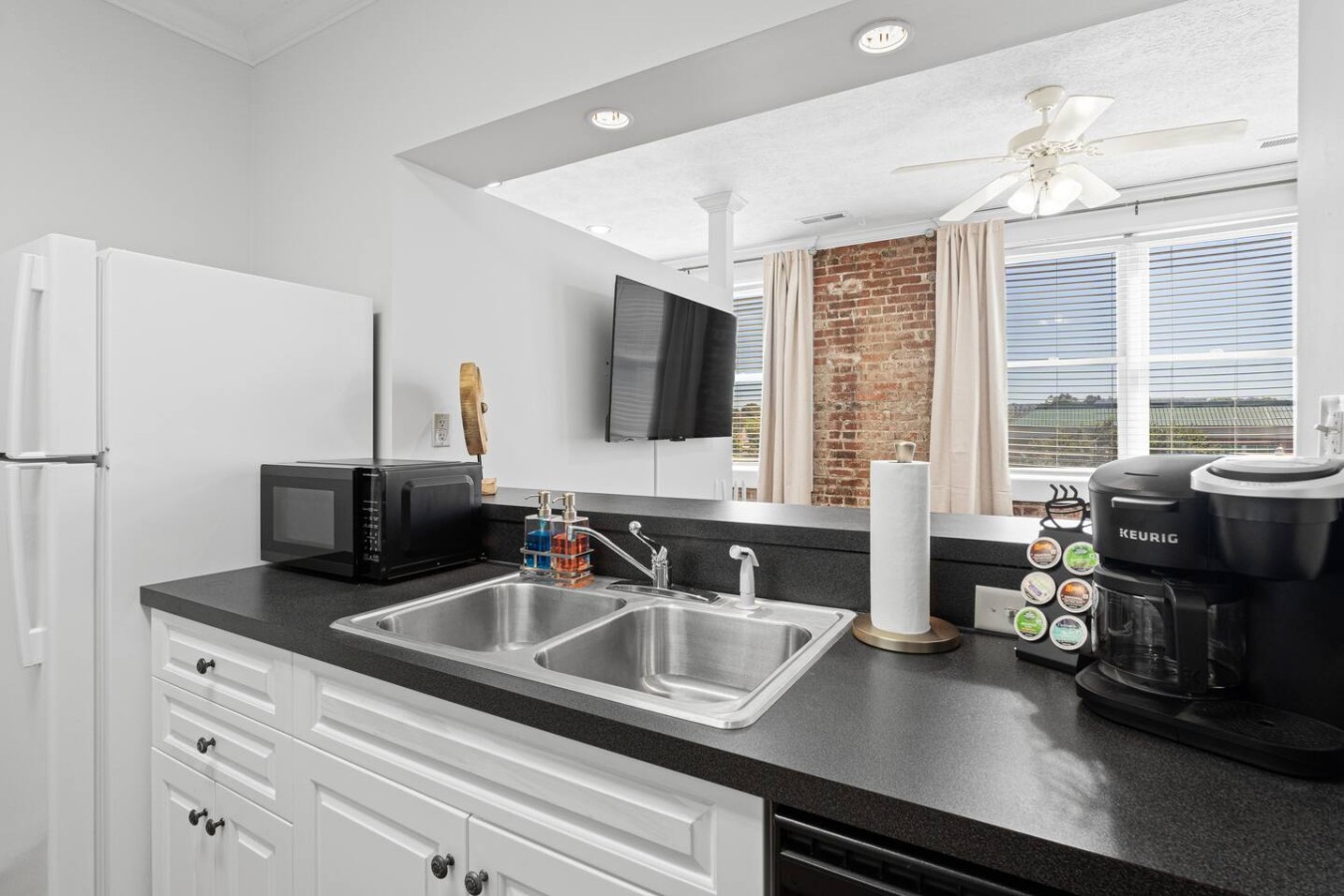 This open-concept kitchen offers a convenient view into the living space, making meal prep a breeze while staying connected. Equipped with a Keurig coffee maker, microwave, and double sink, this fully stocked kitchen has everything you need for your