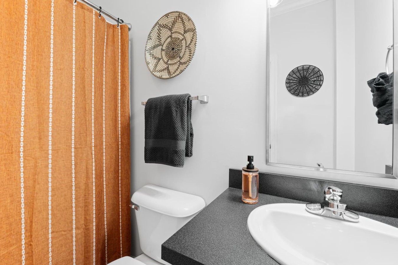 With stylish décor and modern touches, this bathroom features a shower/tub combo with a warm, inviting curtain. Thoughtful accents like the woven wall art add a touch of character, making this space both functional and visually appealing.
