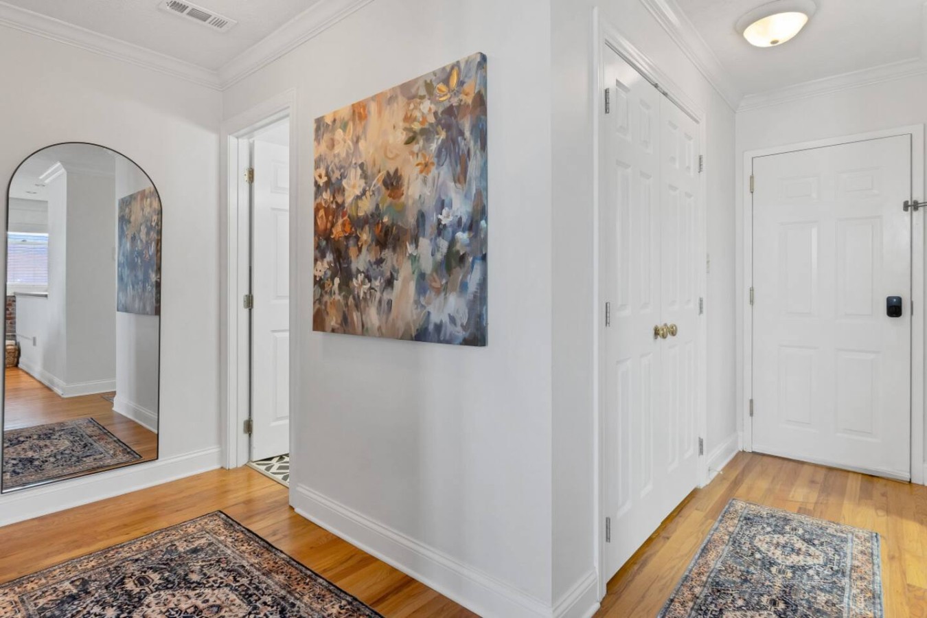 Bright and welcoming entryway featuring hardwood floors, elegant rugs, and a stylish full-length mirror. Thoughtfully decorated with modern artwork, creating a warm and inviting atmosphere as you step into your stay.