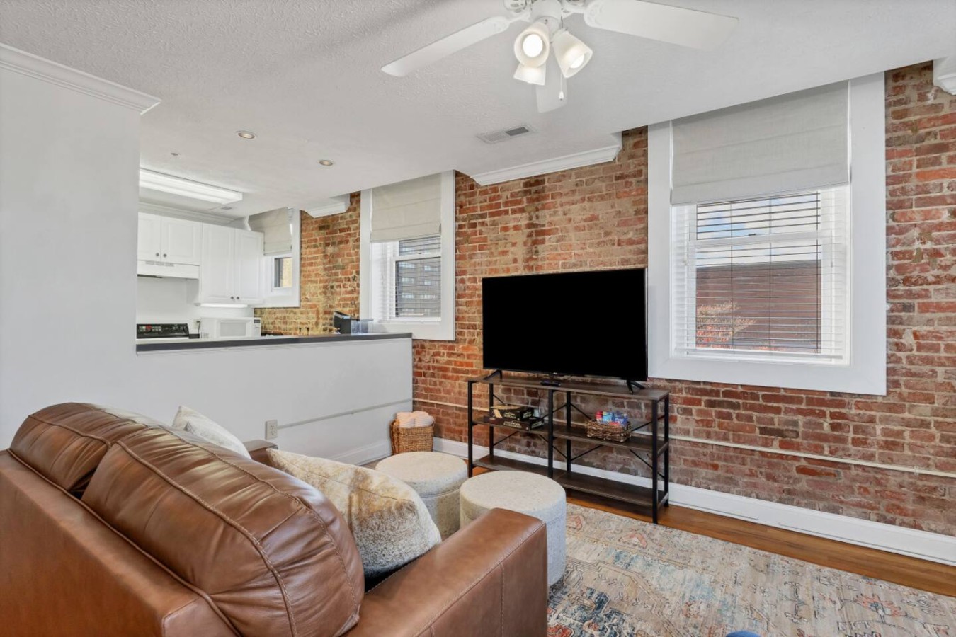Stylish living room with exposed brick walls, a cozy leather sofa, and a large TV for entertainment. Natural light fills the space, creating a warm and inviting atmosphere. Perfect for relaxing after exploring downtown or enjoying a movie night in.