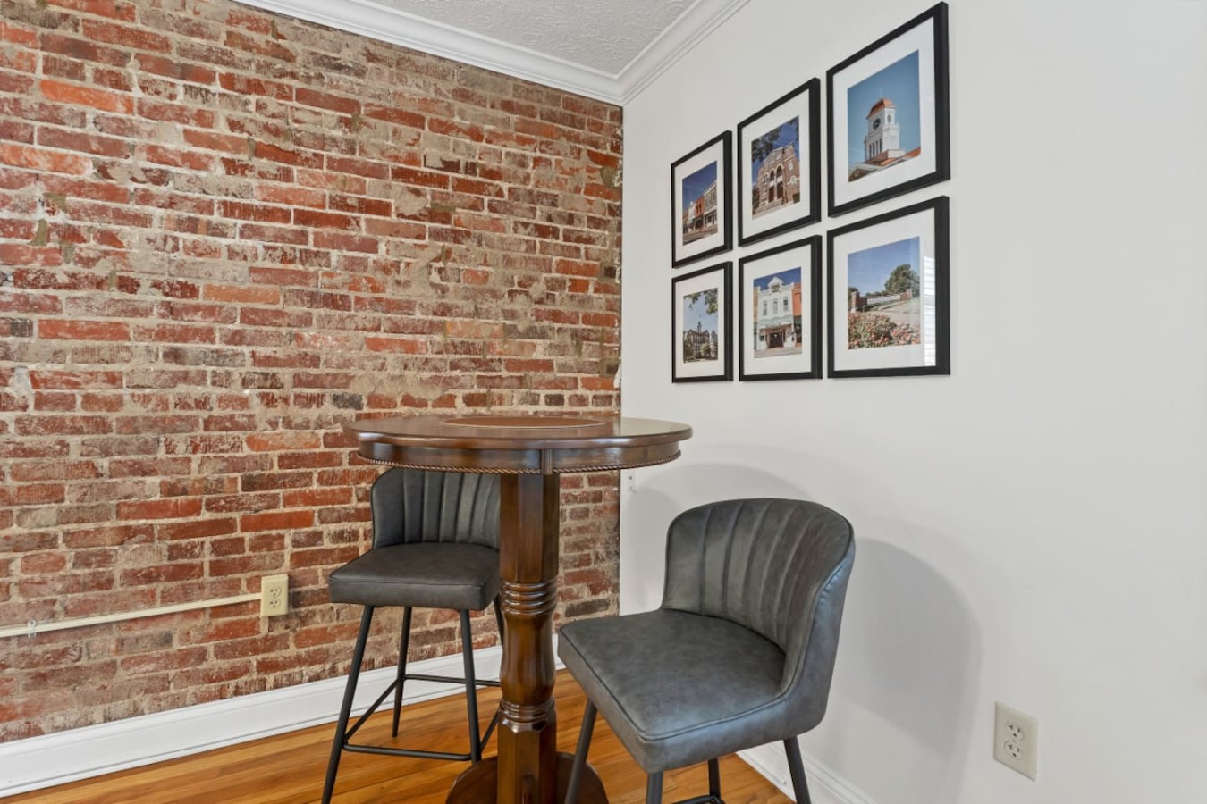 Cozy dining nook with exposed brick walls, stylish framed artwork, and a chic bistro table with plush seating. A perfect spot to enjoy coffee, meals, or a glass of wine while soaking in the charming ambiance of this thoughtfully designed space.
