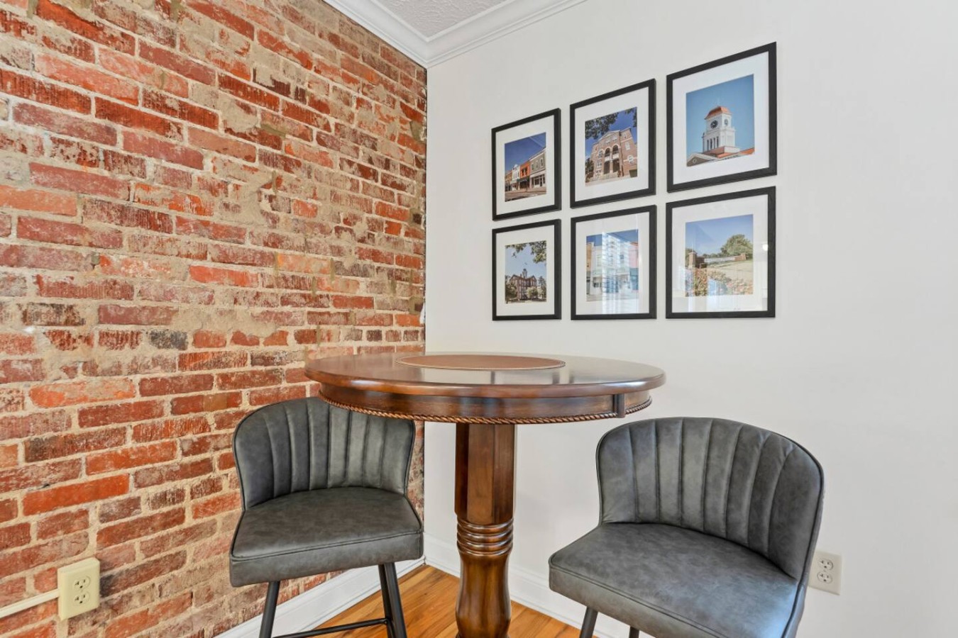 Cozy dining nook with a stylish high-top table, exposed brick, and framed local artwork. A perfect spot to enjoy coffee or a meal while soaking in the charming ambiance.