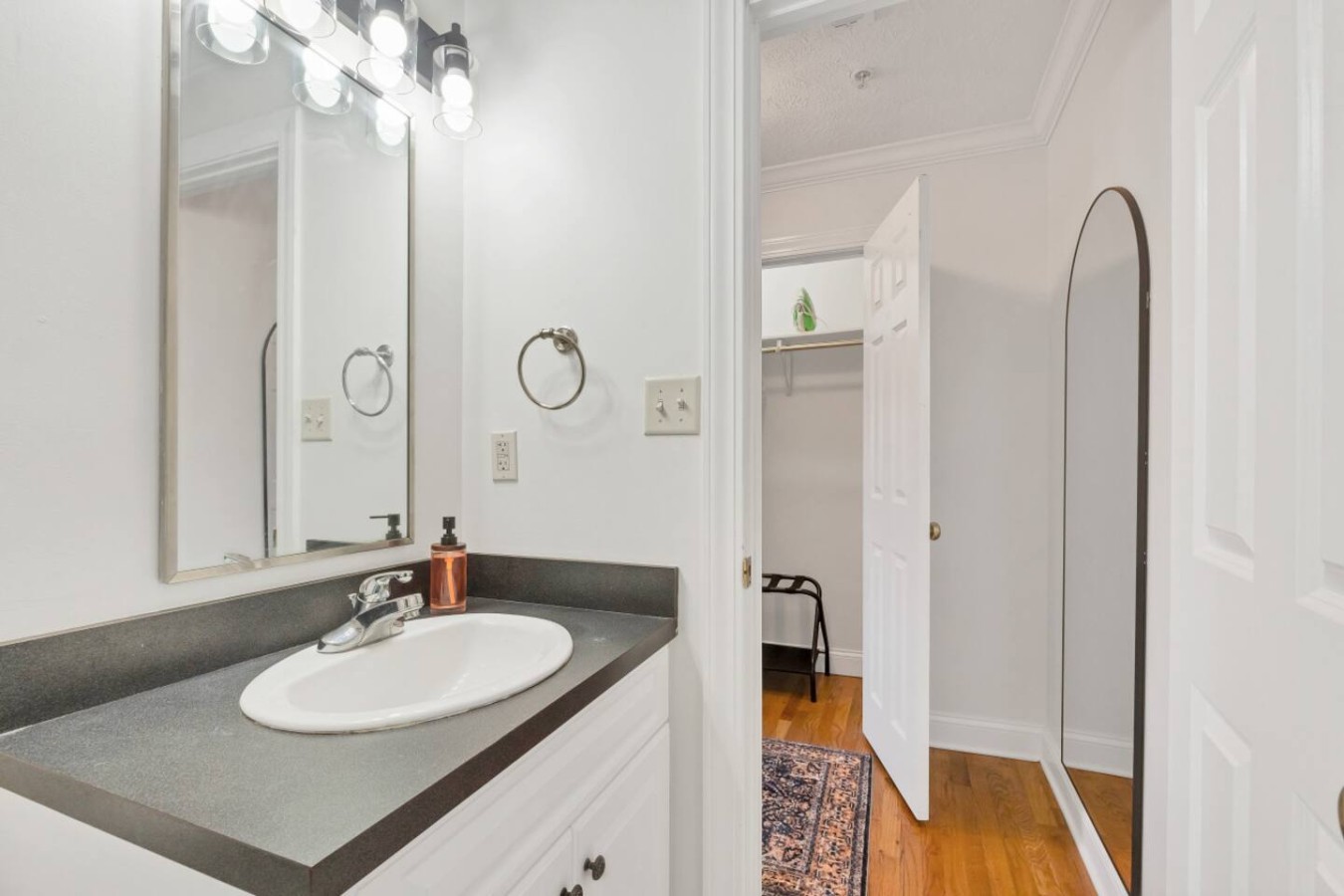Modern bathroom with sleek black countertops, a well-lit vanity mirror, and a spacious walk-in closet. A clean and stylish space designed for comfort and convenience during your stay.