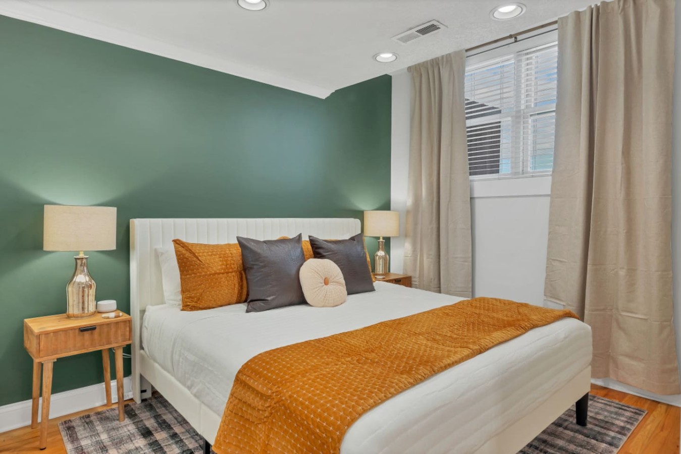 Relax in this stylish bedroom featuring a plush king bed, cozy linens, and a soothing green accent wall. Natural light flows through the window, creating a serene retreat in the heart of downtown Maryville.