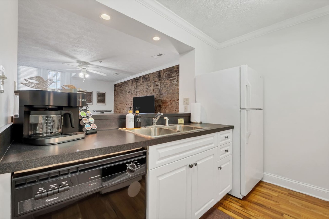 Open-concept kitchen with a dishwasher, full-size fridge, and stocked coffee bar. Overlooks the cozy living space with exposed brick, creating a seamless flow for entertaining or relaxing with a fresh brew.