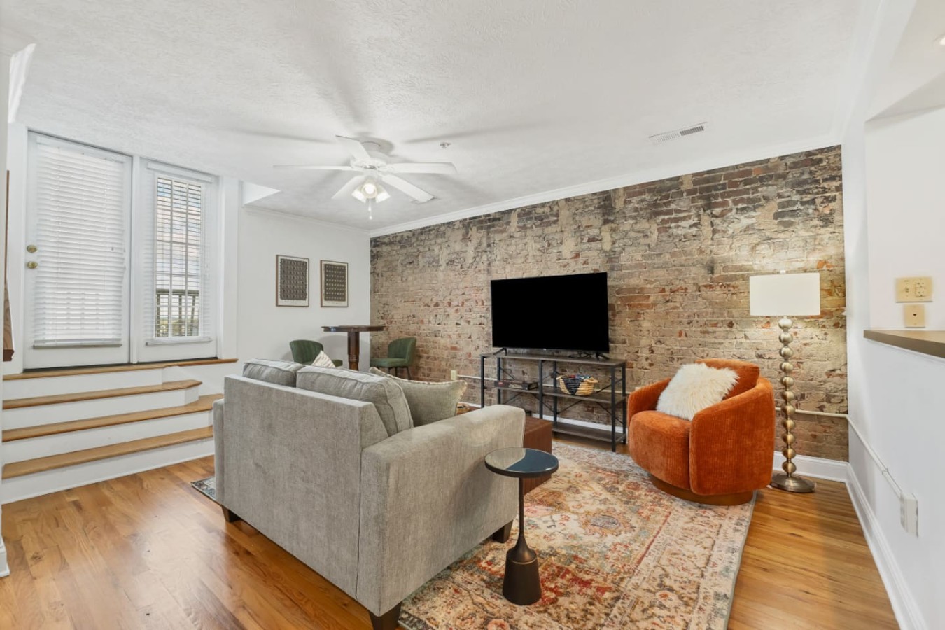 Stylish living room with exposed brick, cozy seating and a large TV. Natural light pours in from the private balcony entrance, creating a warm and inviting space. Perfect for unwinding after a day exploring downtown Maryville’s shops and restaurants.