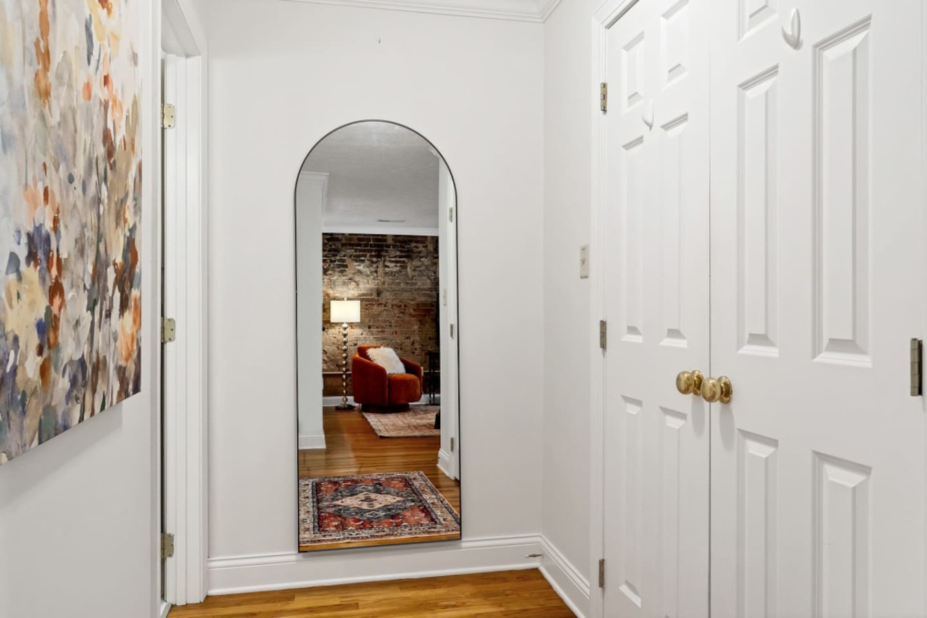 Bright hallway featuring a stylish arched mirror, warm hardwood floors, and modern decor leading to the cozy living space.