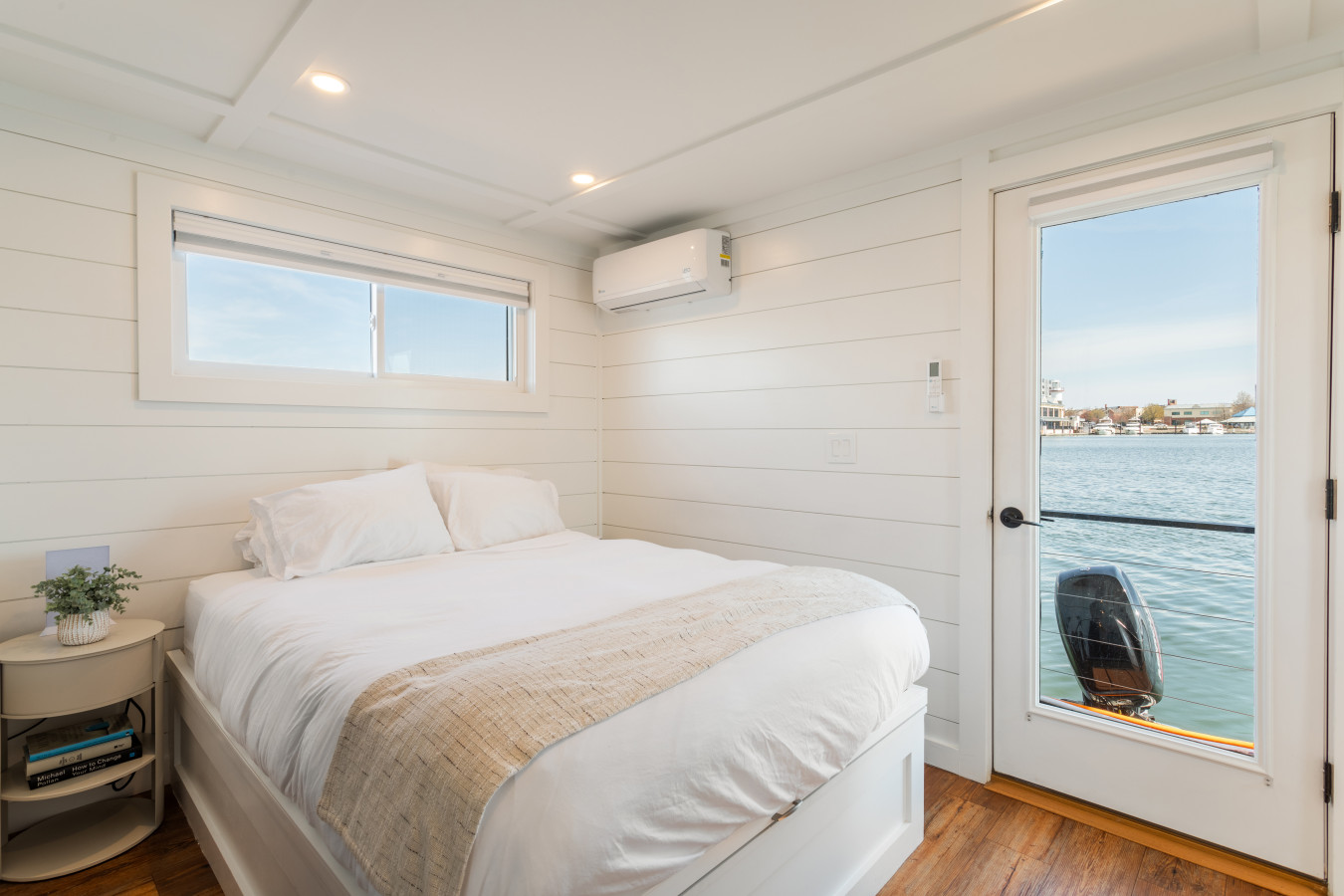 Wake up to water — this cozy queen bedroom features white shiplap, luxury bedding, and a glass door with harbor views.