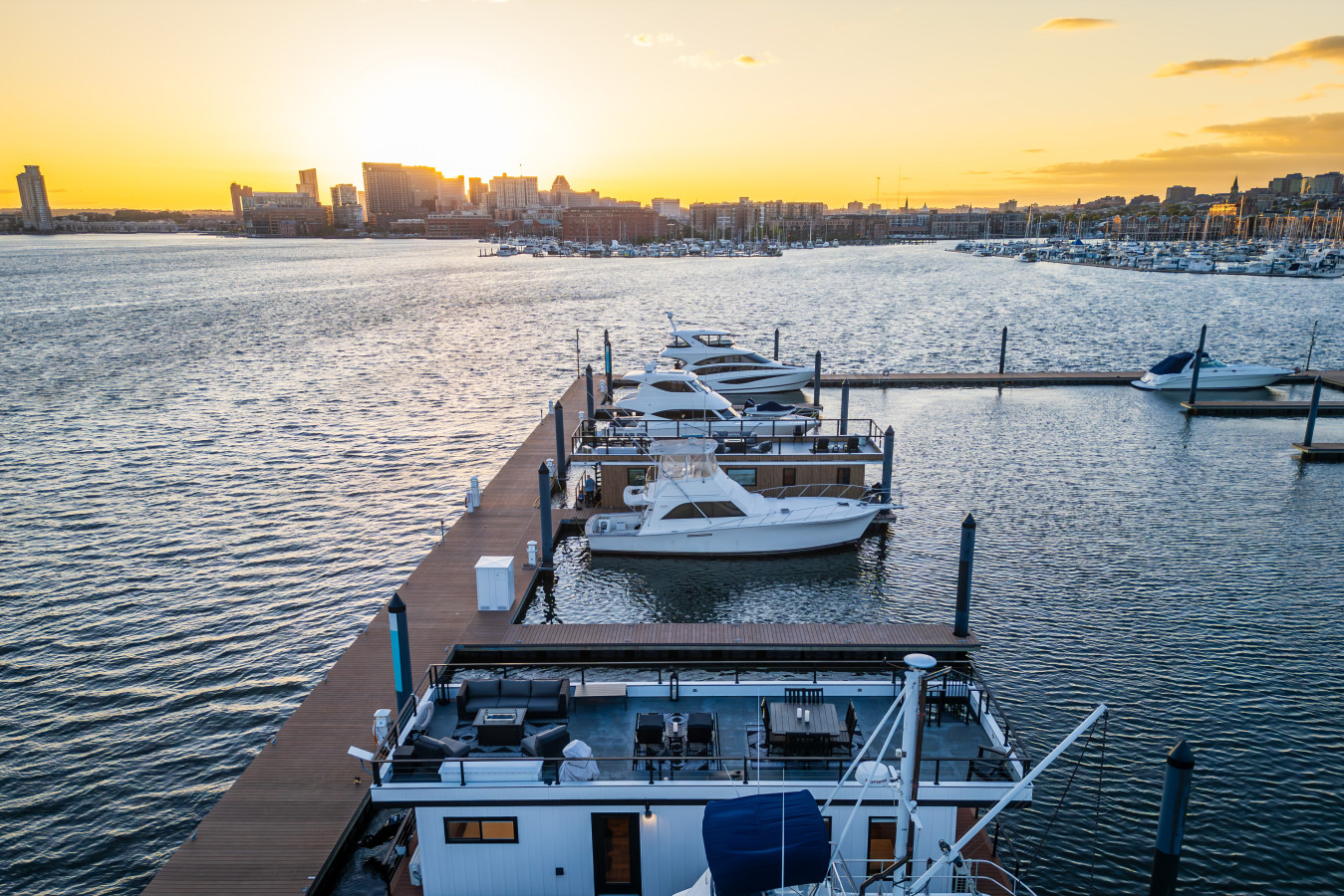 Drone view of our private marina at sunset — houseboats and yachts line the dock with Baltimore skyline glowing in the background.
