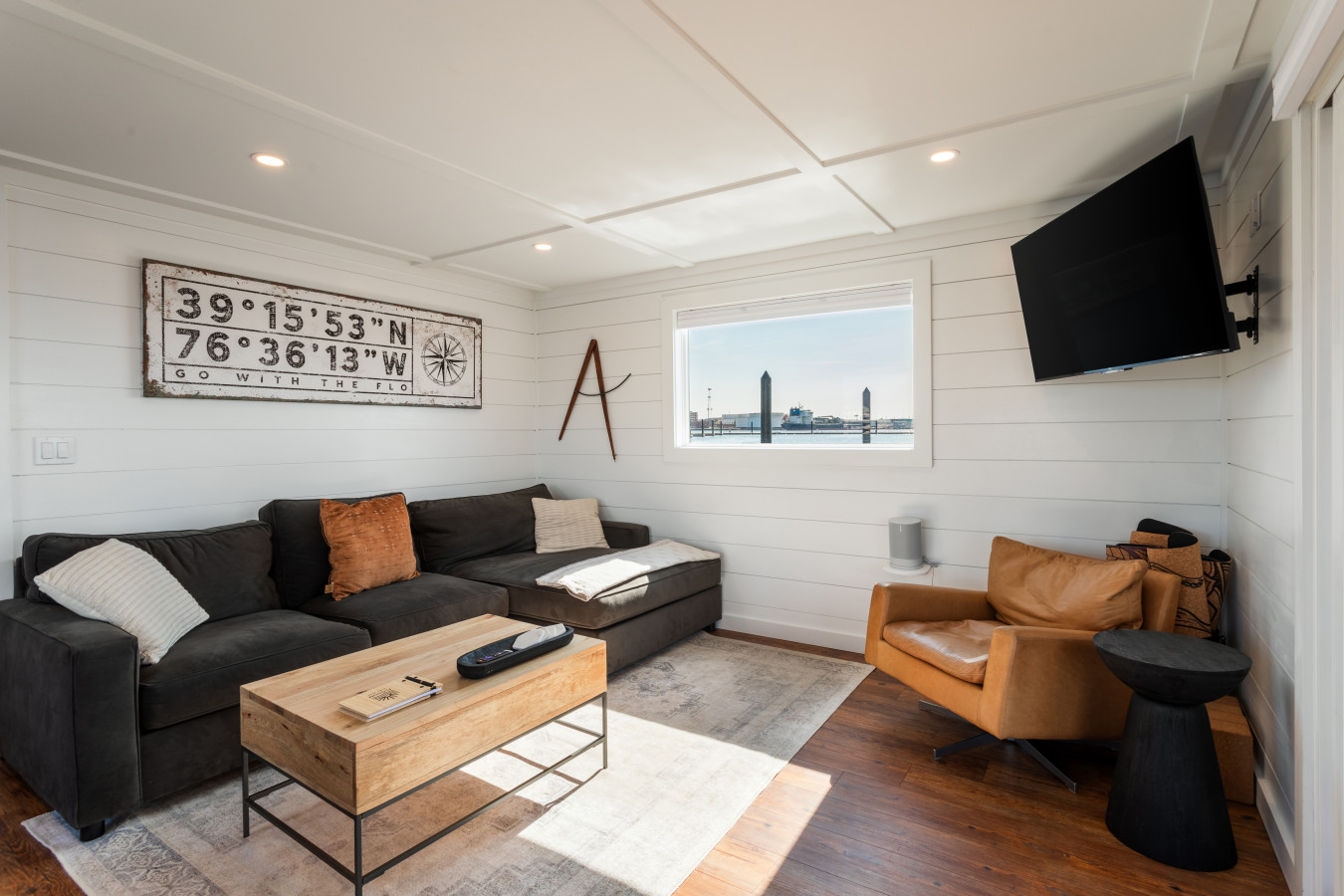 Kick back on the plush sectional or leather chair — smart TV, harbor views through the window, and cozy nautical vibes.