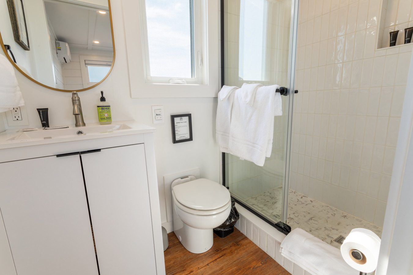 The second bath keeps it clean and stylish — gold mirror, white vanity, glass shower, and warm hardwood floors.