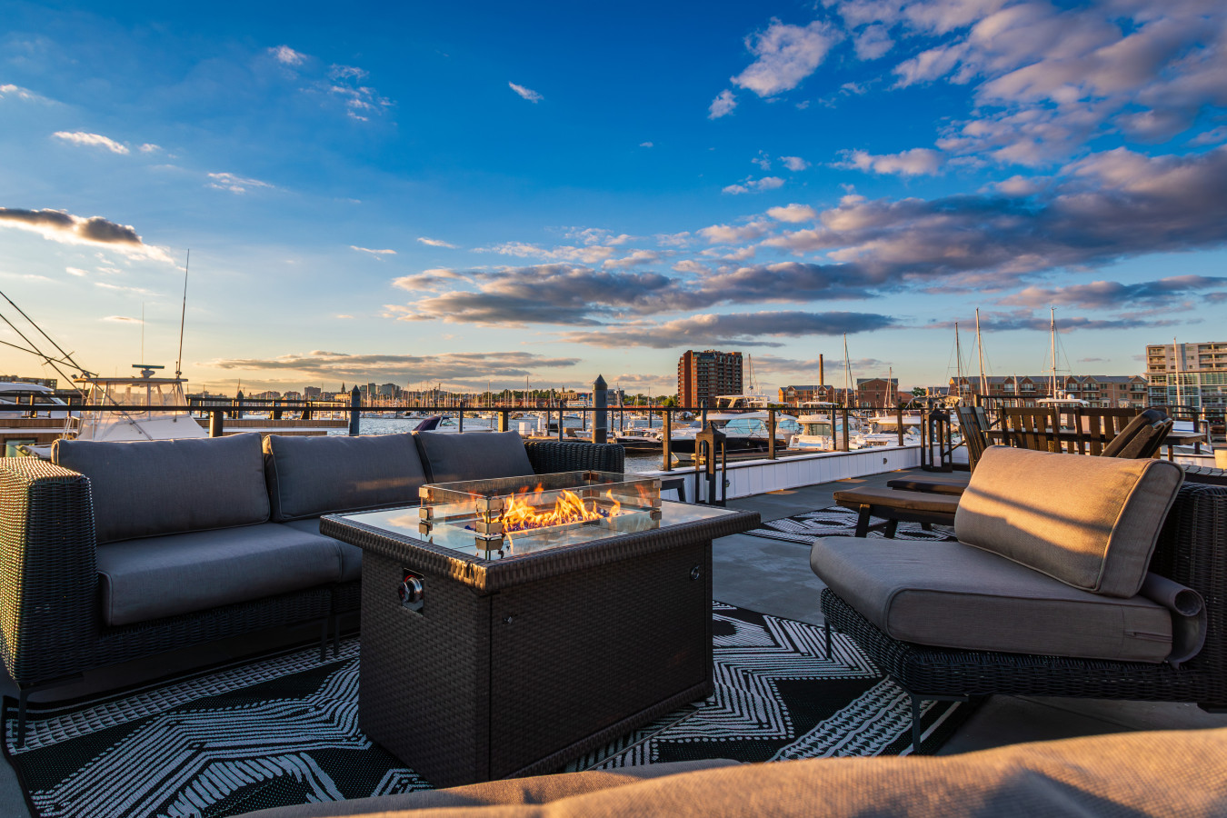 Flames flicker at dusk on the rooftop — sink into deep cushions with the Baltimore skyline and marina boats as your backdrop.