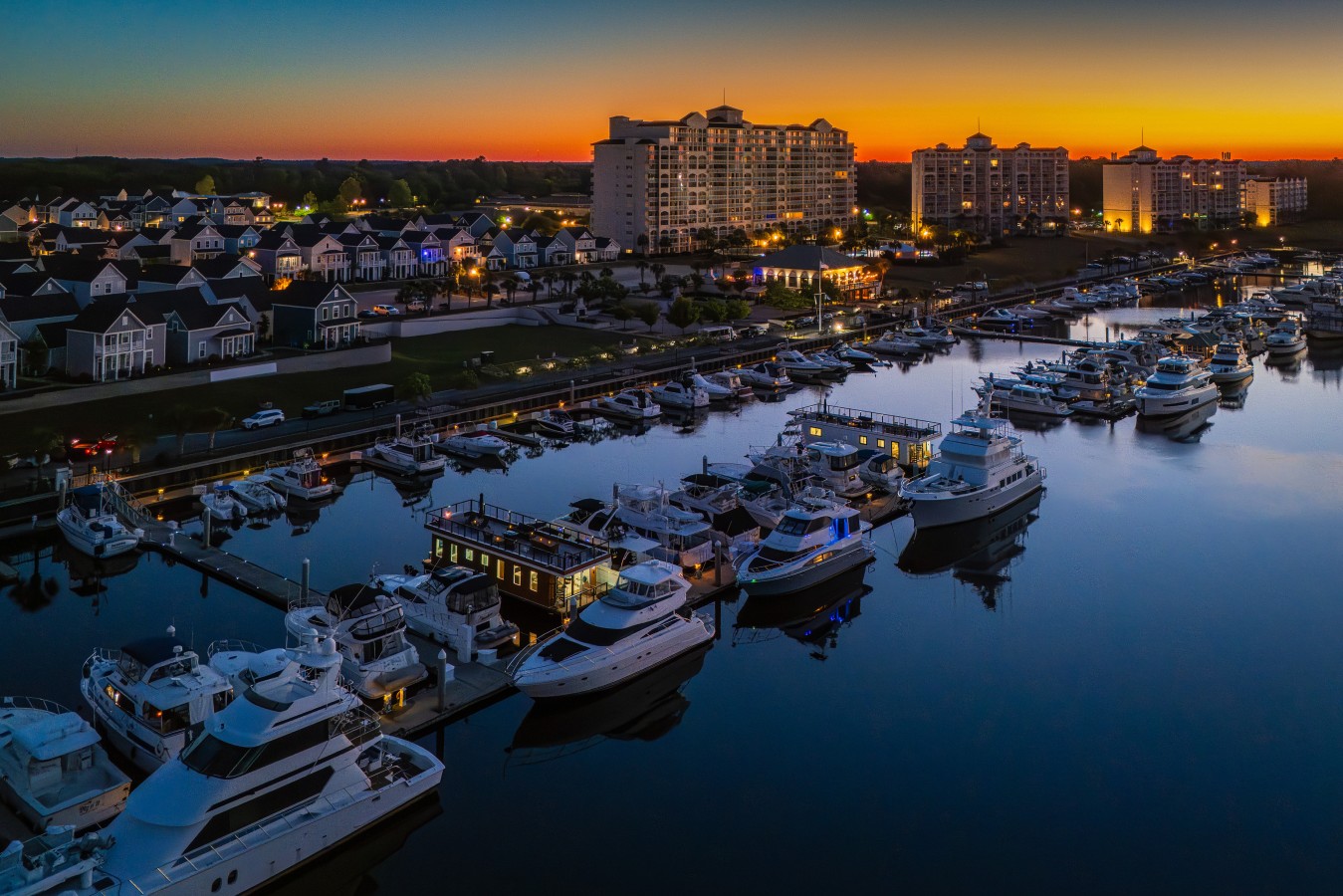 An aerial view of Barefoot Marina at blue hour, with Palmera glowing among the yachts and the Barefoot Resort towers lit against the pre-dawn horizon.