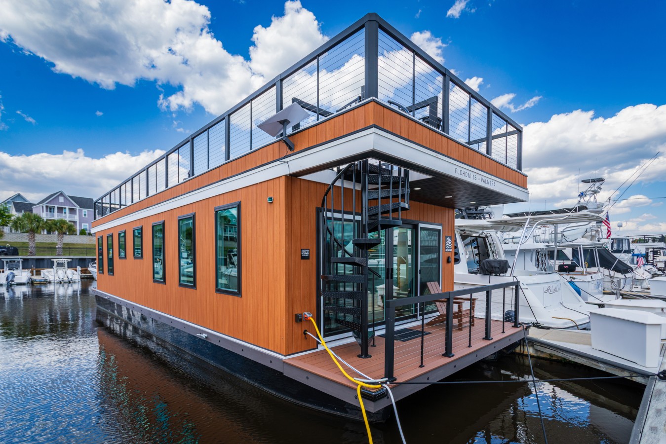 Palmera's warm cedar exterior at Barefoot Marina, with the entry deck, spiral staircase to the rooftop, and floor-to-ceiling windows framing the Intracoastal under a dramatic Carolina sky.