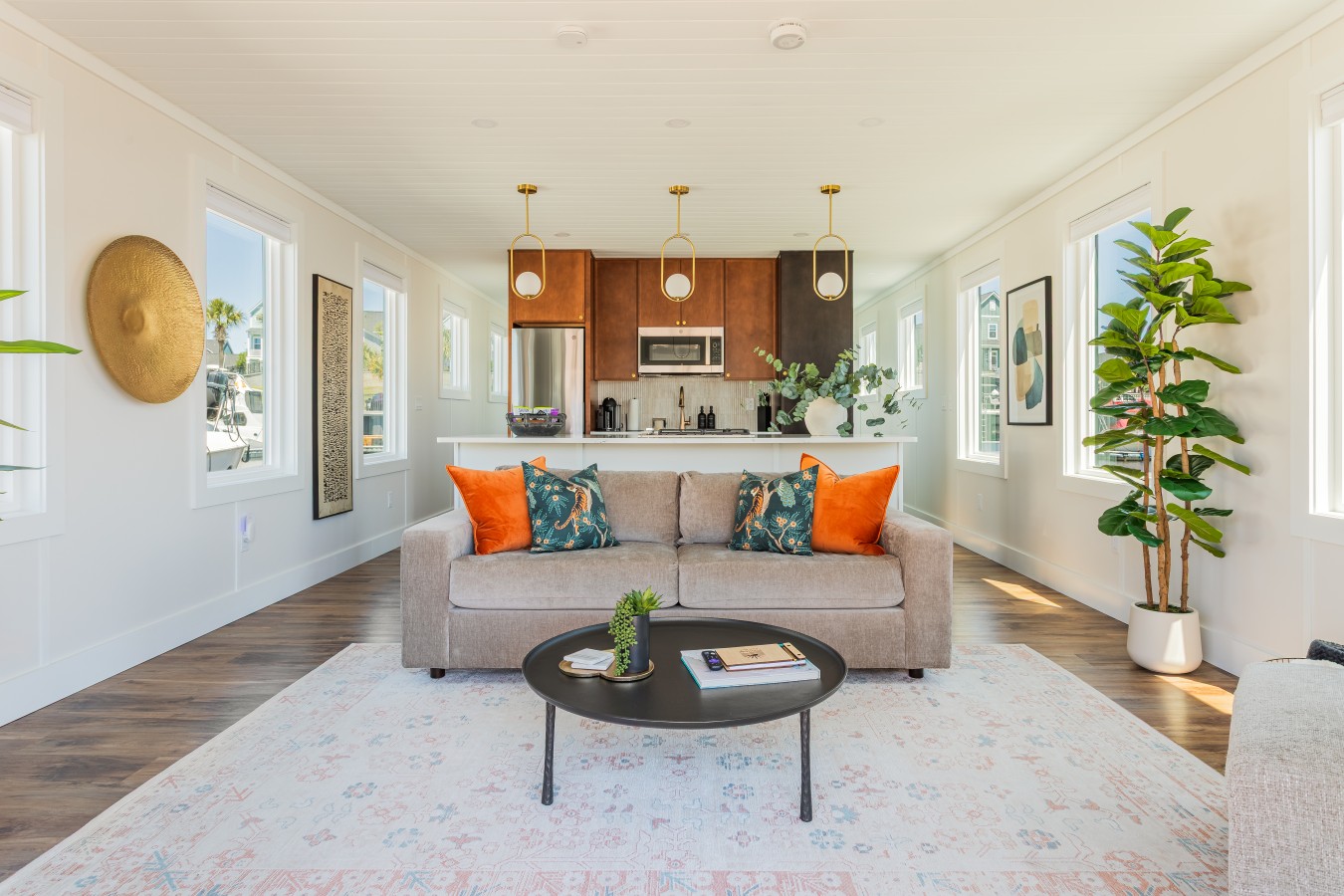 Sun-filled living area with the designer sofa, gold pendant lighting over the kitchen, waterway views through every window, and natural light pouring across the open-plan layout.