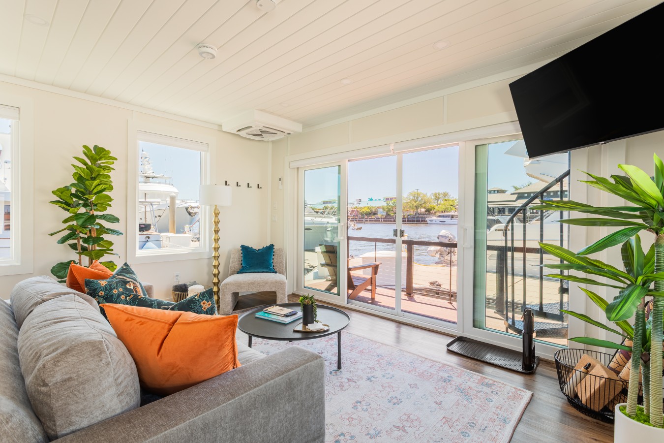 Living area looking out through the sliding glass doors to the front deck, the marina, and the Intracoastal Waterway, with afternoon light filling the space from every angle.